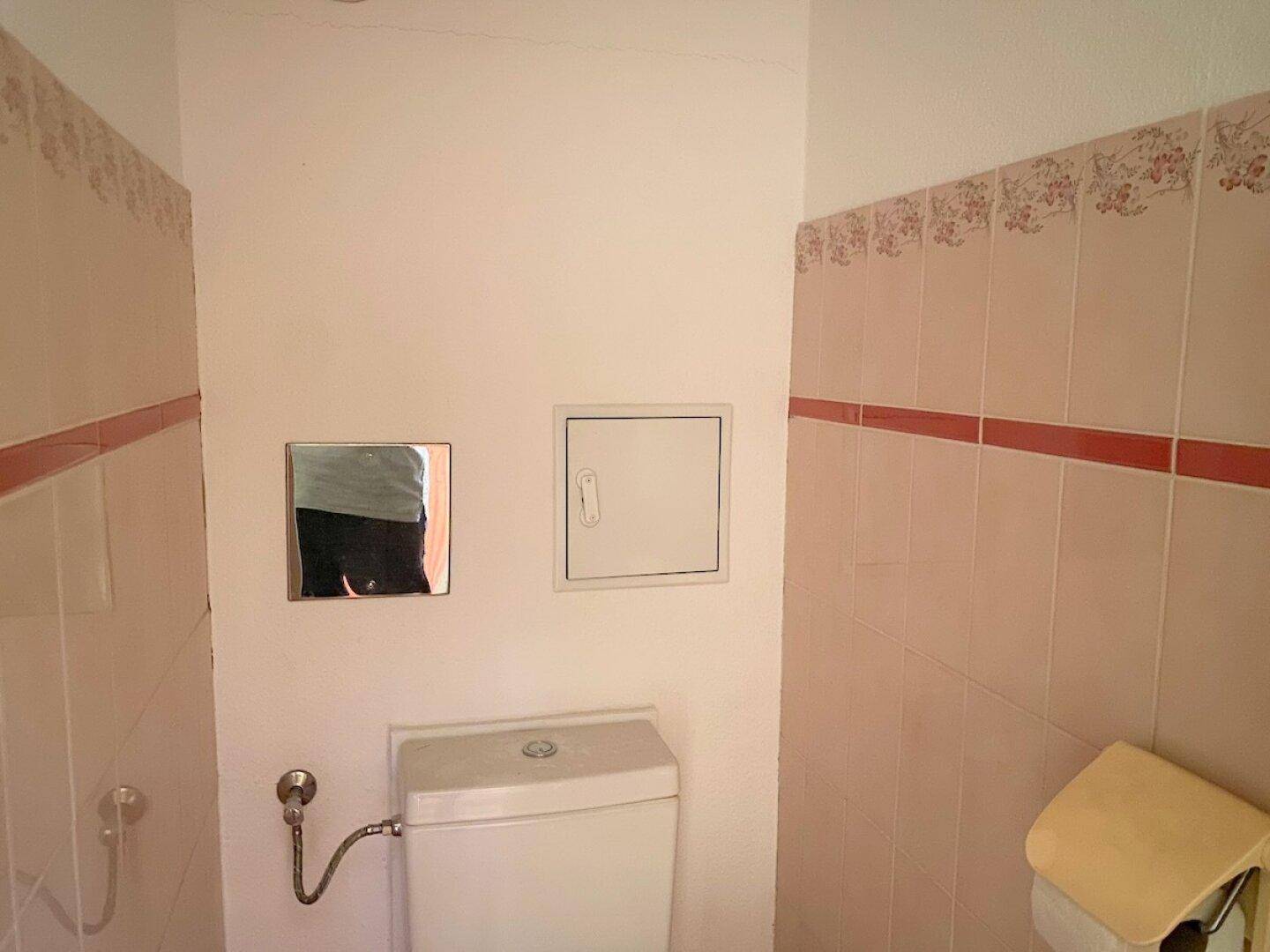 Kleines Gäste-WC mit einfacher Toilette und Wandfliesen in Pastellfarben.