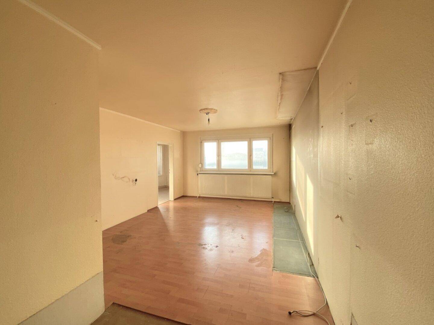 Helles Wohnzimmer mit Laminatboden und großen Fenstern, die viel Tageslicht hereinlassen.