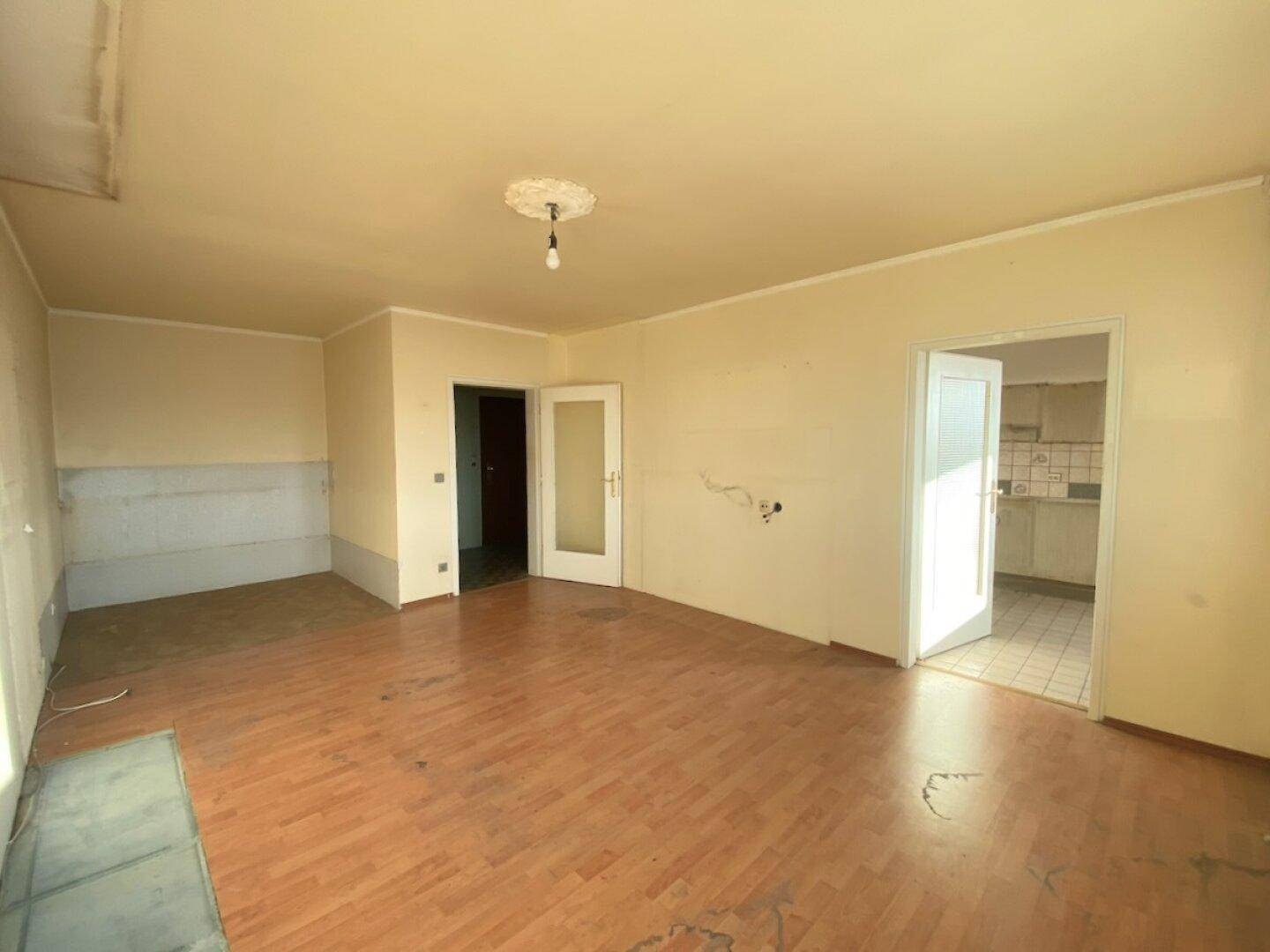 Geräumiges Wohnzimmer mit abgenutztem Laminatboden und unfertigen Wänden, bereit zur Renovierung.