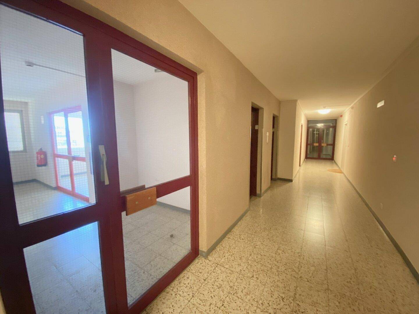 Langer Gemeinschaftsflur in einem Wohngebäude mit Fliesenboden und mehreren Wohnungstüren.