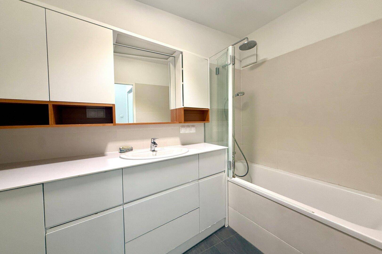 Modernes Badezimmer mit weißem Waschtisch, Spiegelschrank und Badewanne mit Duschfunktion.