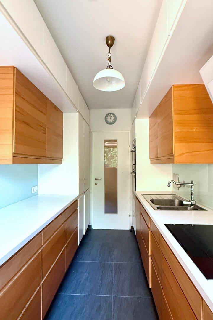 Schmale, funktionale Küche mit Holzschränken, dunklem Fliesenboden und integrierten Geräten.