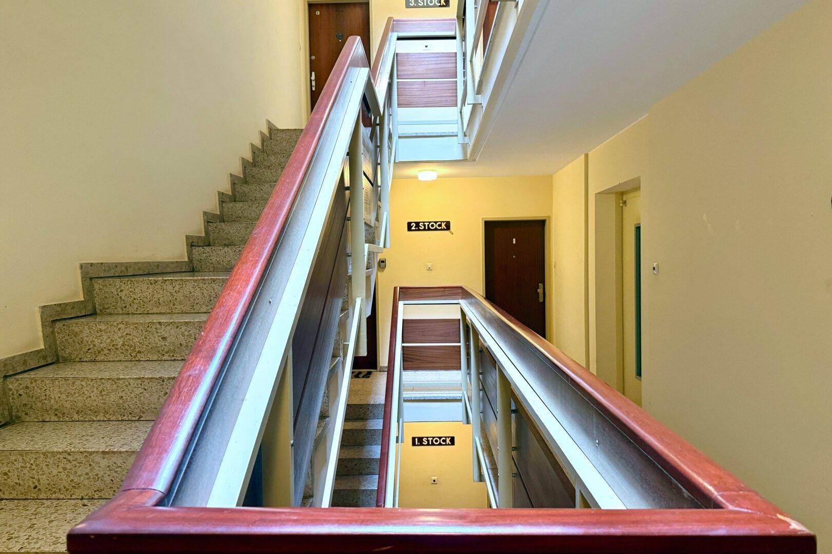 Helles Treppenhaus mit Steinstufen und Holzgeländer, verbindet die verschiedenen Stockwerke.