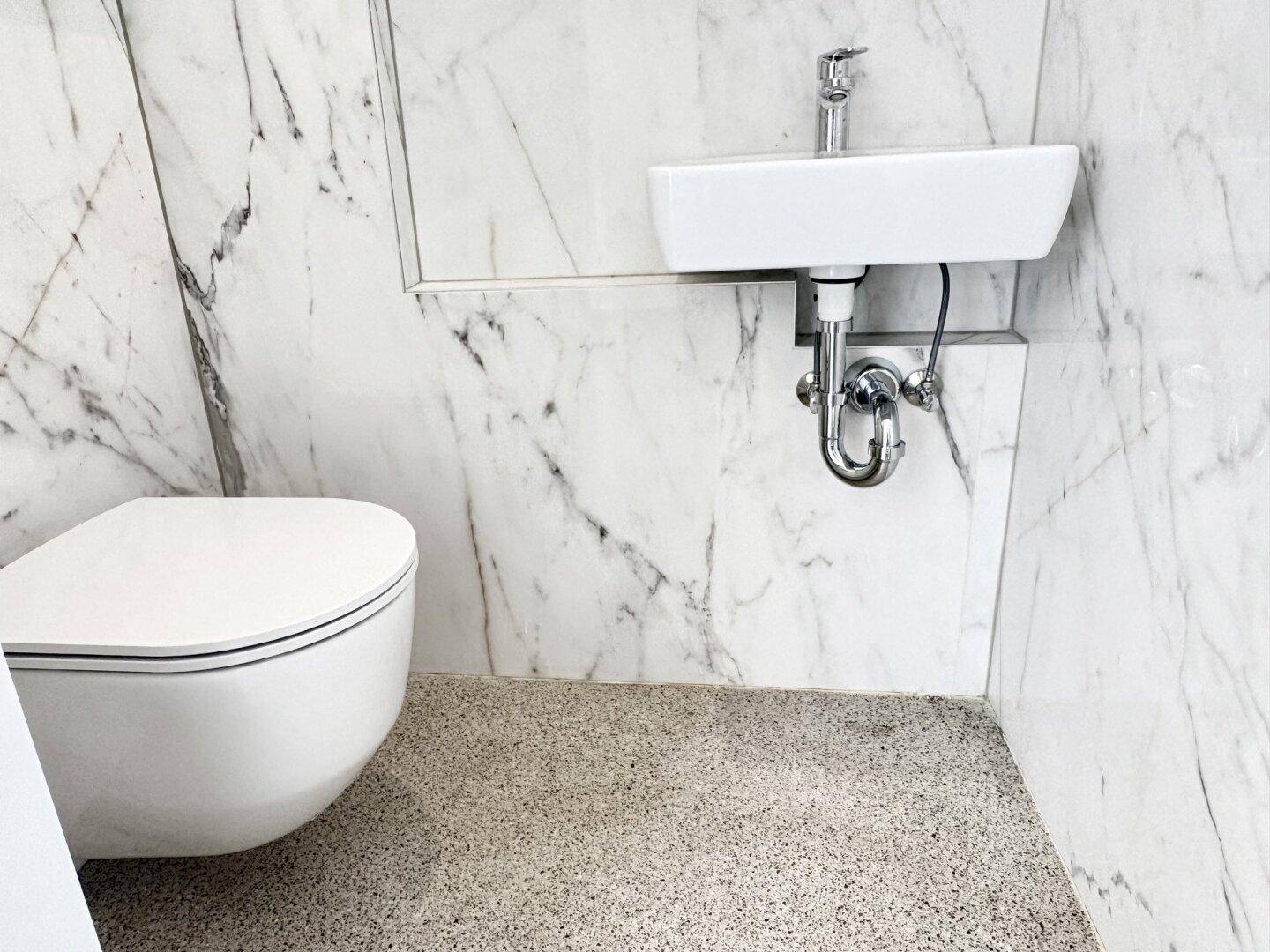 Modernes Badezimmer mit Marmorfliesen, wandhängendem WC und kleinem Waschbecken.