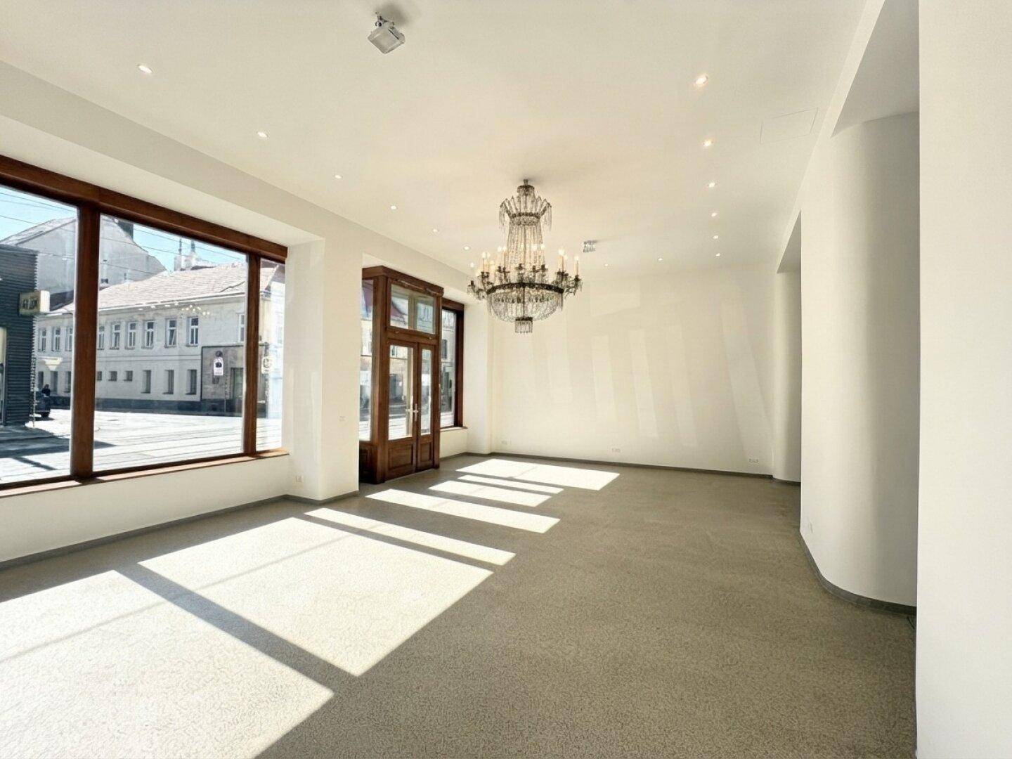 Großer, heller Gewerberaum mit viel Tageslicht, hohen Decken und einem eleganten Kronleuchter.