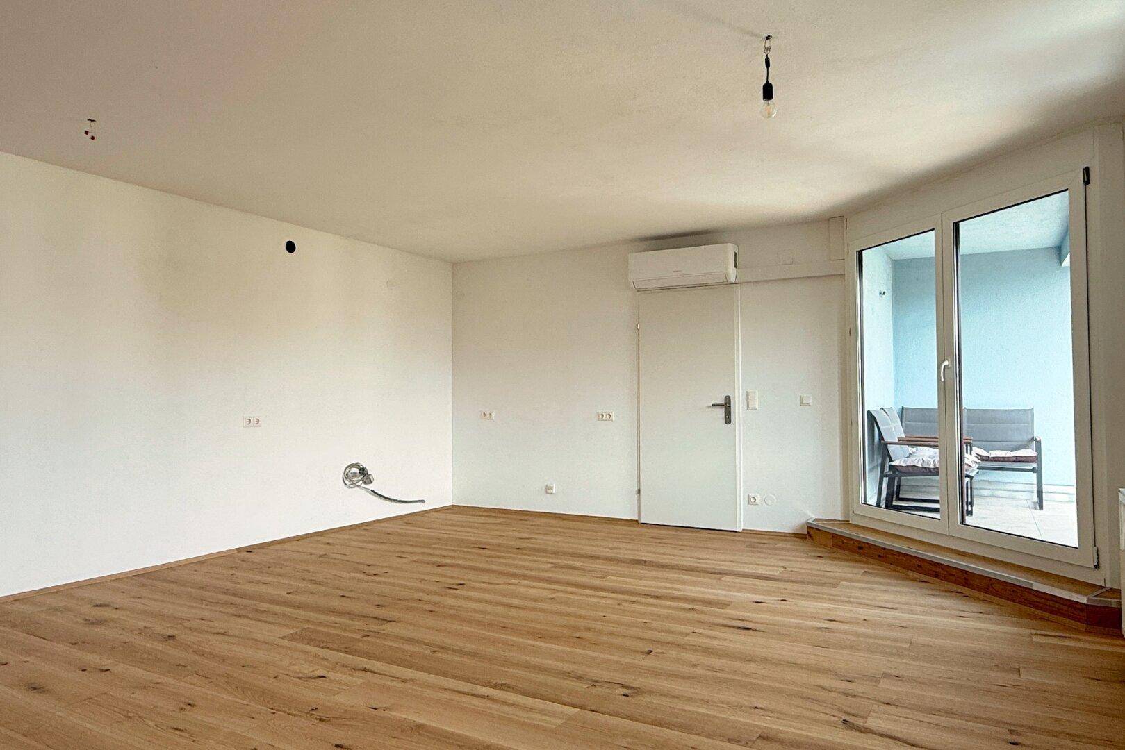 Heller, leerer Raum mit neuem Holzboden, weißen Wänden, Klimaanlage und Zugang zum Balkon.