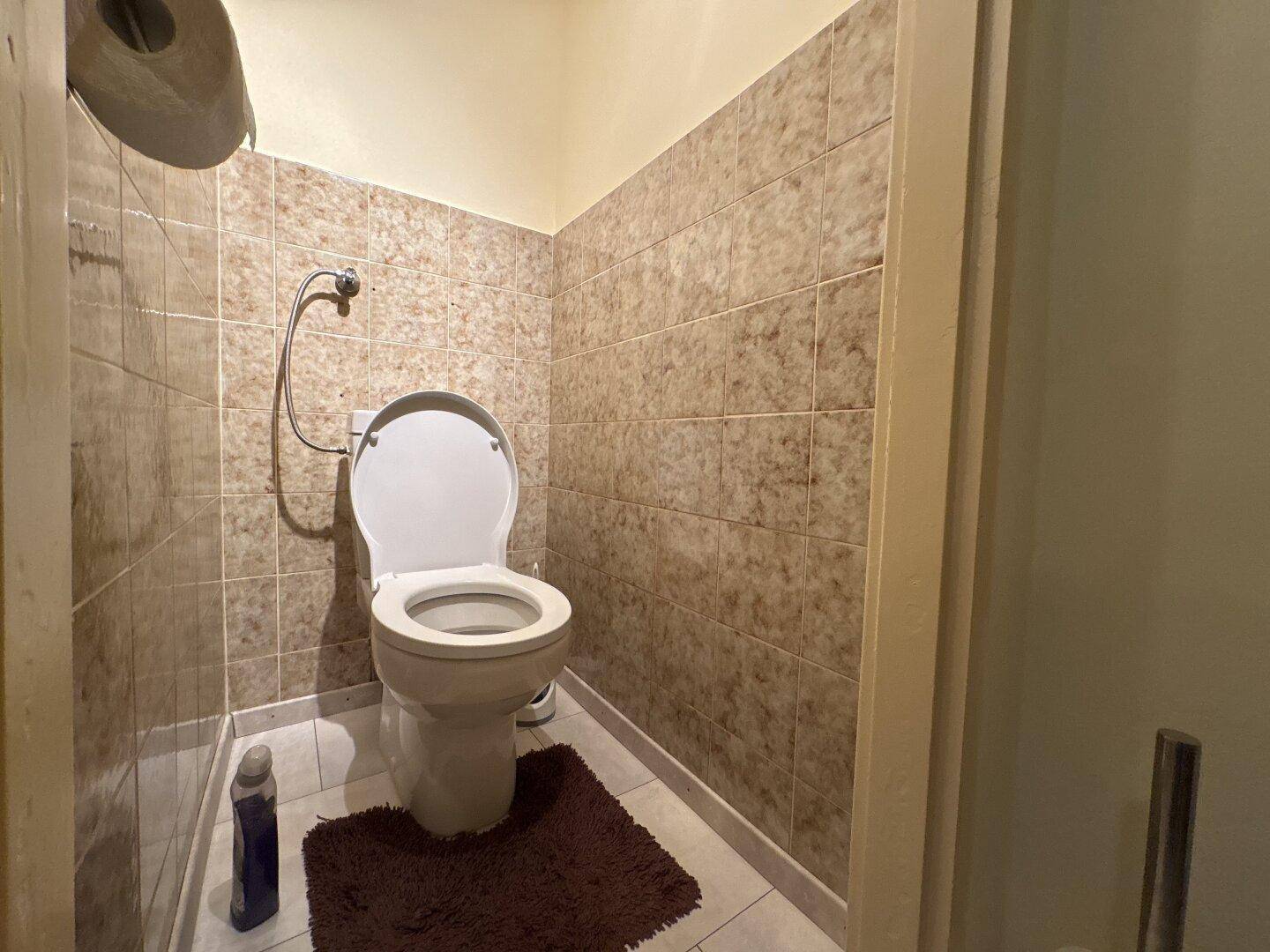 Separate Toilette mit Fliesen an den Wänden und einem einfachen WC, funktional gestaltet.