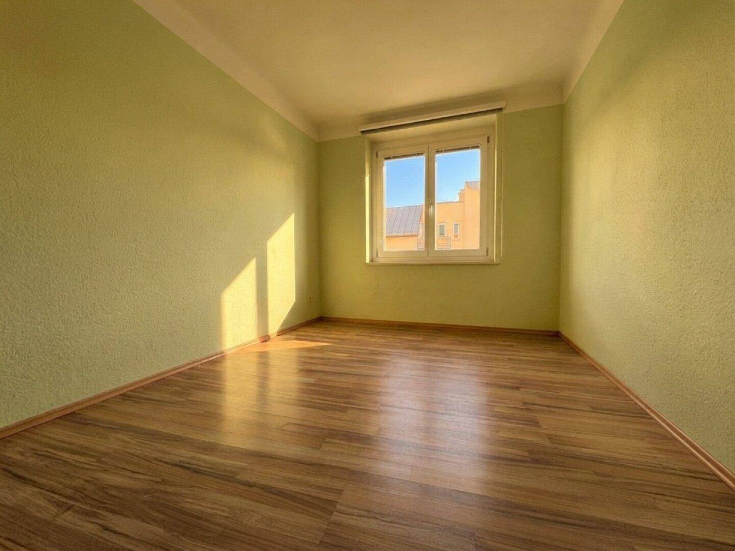 Sonniger Raum mit hellgrünen Wänden und Laminatboden, ideal als Schlaf- oder Kinderzimmer.