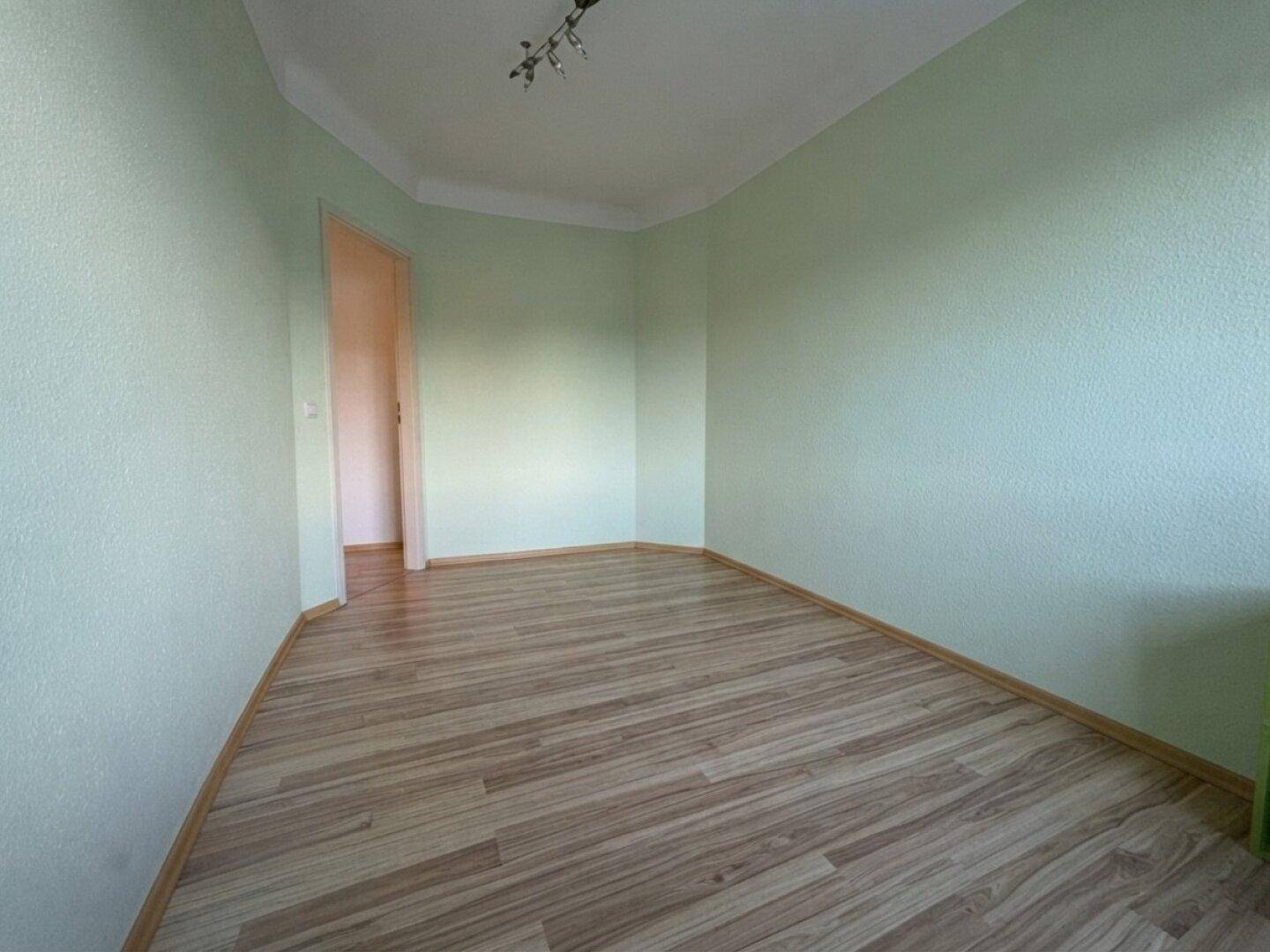 Leeres Zimmer mit hellgrünen Wänden und Laminatboden, bietet vielseitige Einrichtungsmöglichkeiten.