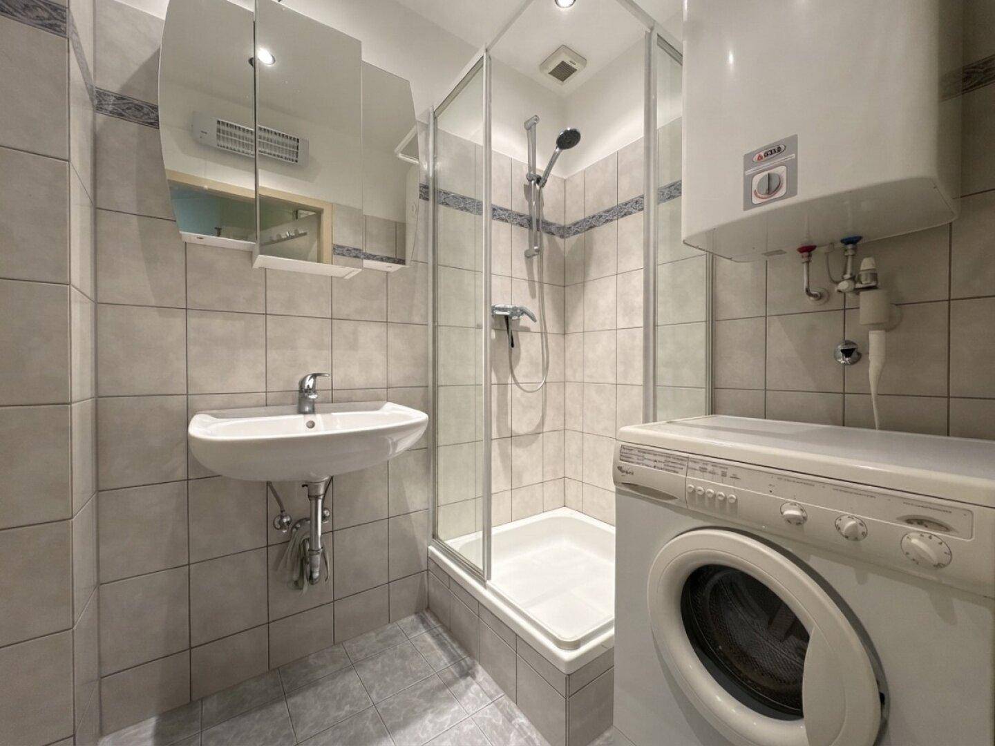 Helles Badezimmer mit Dusche, Waschbecken und Waschmaschine, praktisch und funktional.