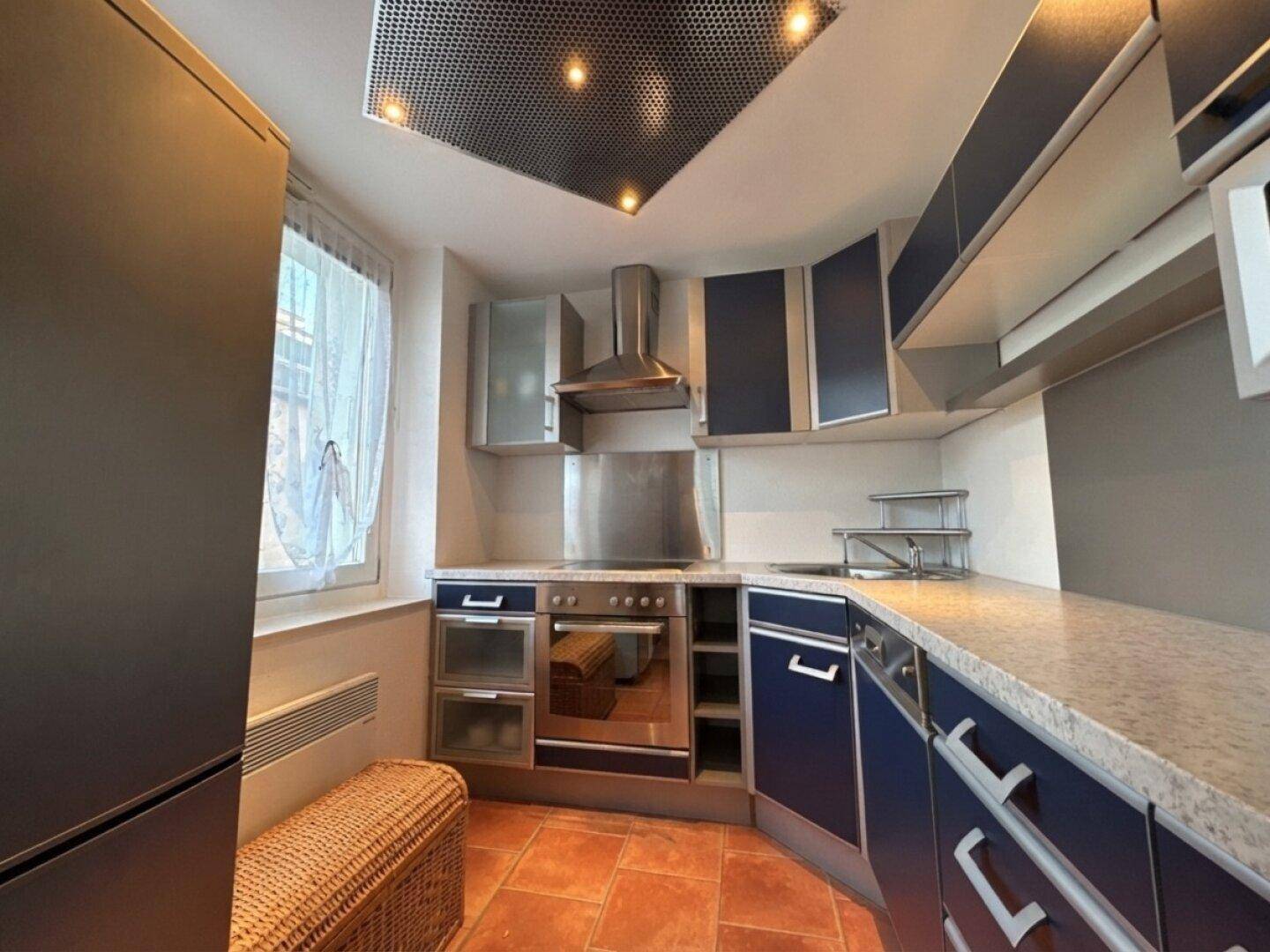 Funktionale Küche mit blauen Schränken, Granitarbeitsplatte und Terrakotta-Fliesenboden.