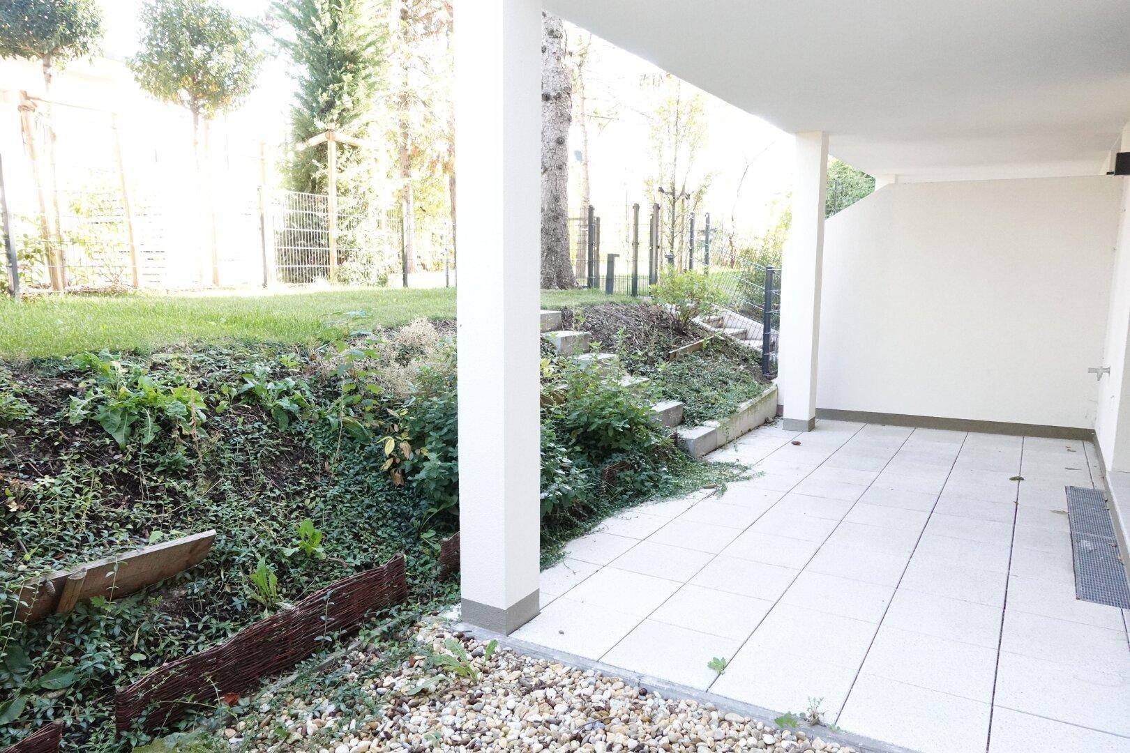 Helle Terrasse mit Fliesenboden und Stufen, die zu einem begrünten Hang führen.