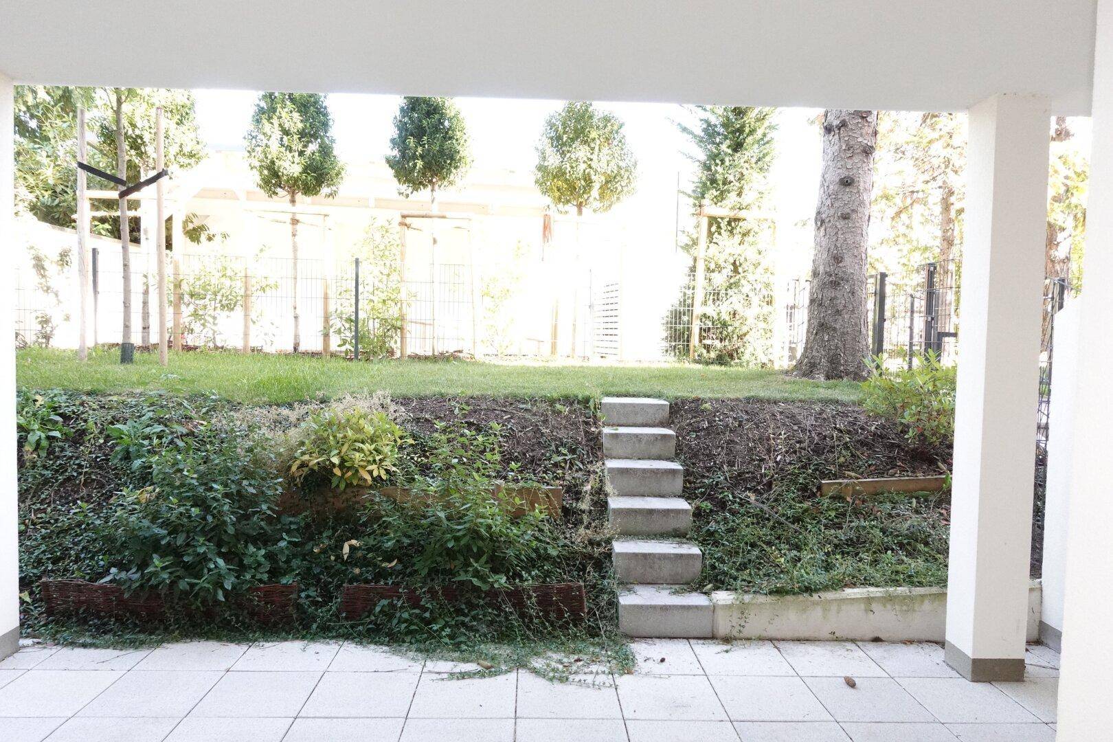 Überdachte Terrasse mit Fliesenboden und Treppe zum erhöhten Gartenbereich.