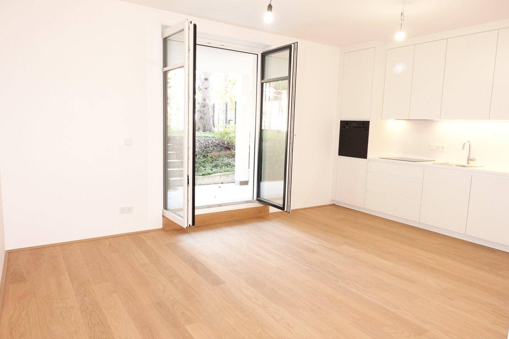 Heller Wohnbereich mit offener Küche, Holzboden und Zugang zur Terrasse oder zum Garten.
