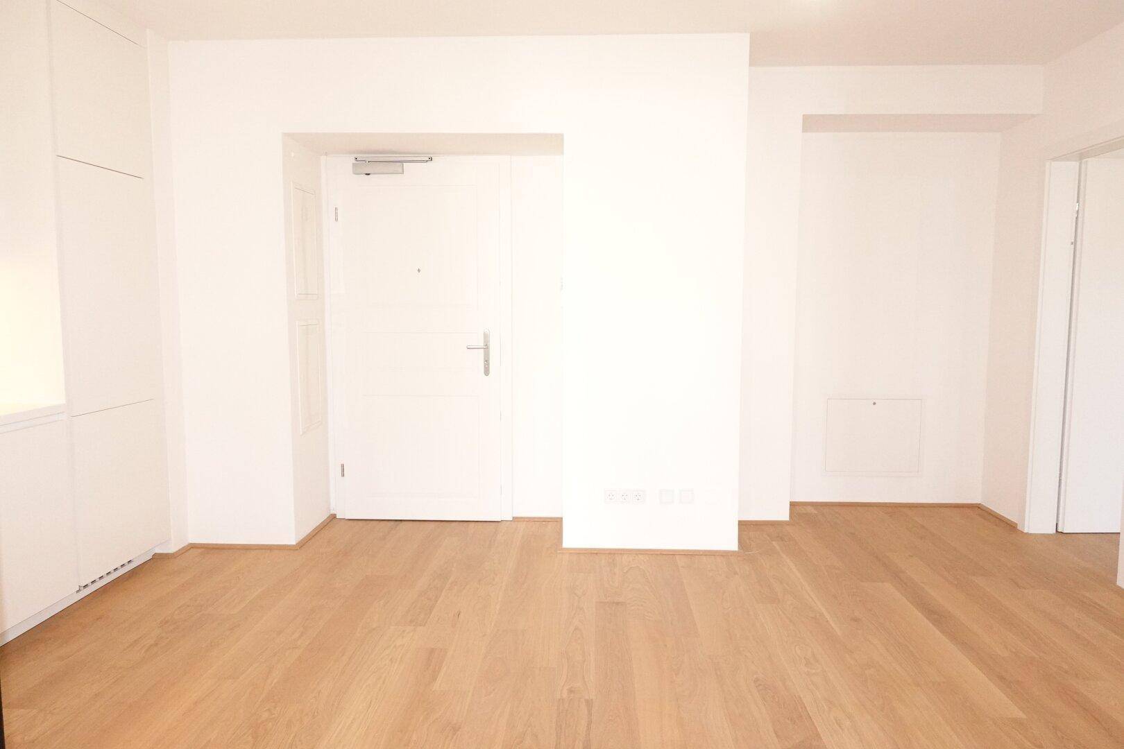 Heller Eingangsbereich mit Holzboden, weißer Tür und integrierten Schränken.