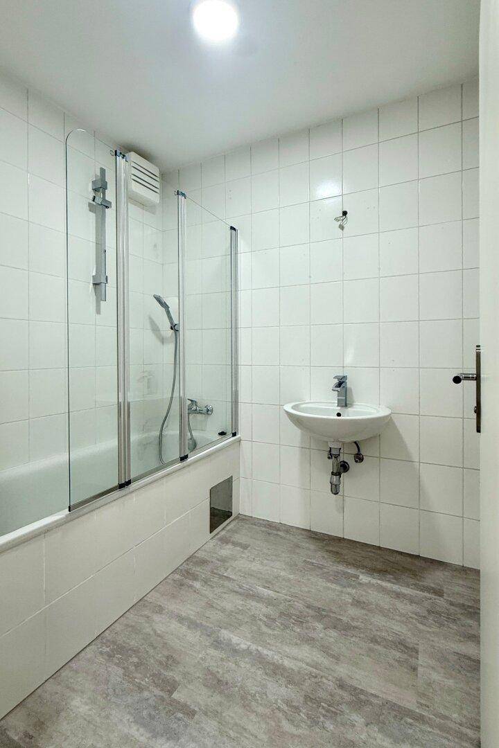 Funktionales Badezimmer mit Badewanne, Duschfunktion und einfachem Waschbecken, hell gefliest und praktisch.