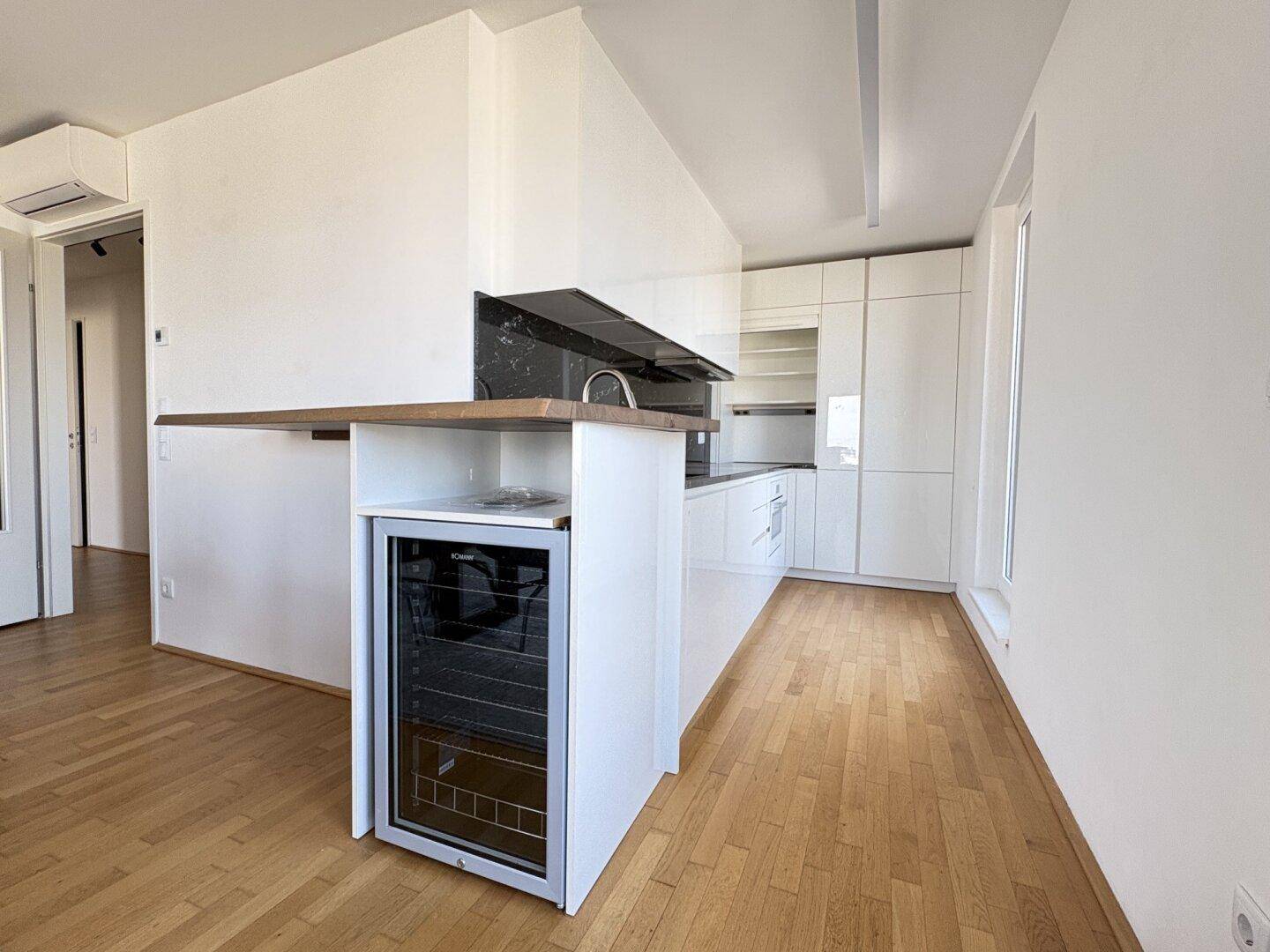 Moderne Einbauküche mit weißen Hochglanzfronten, Holzarbeitsplatte und Weinkühler.