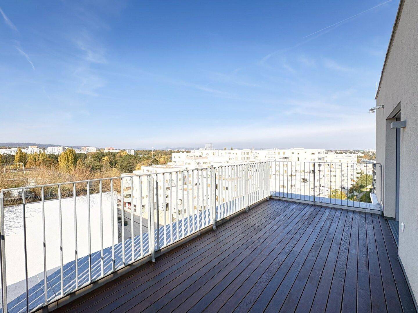 Großer Balkon mit dunklem Holzboden und weitem Blick über die Stadt und die umliegende Landschaft.
