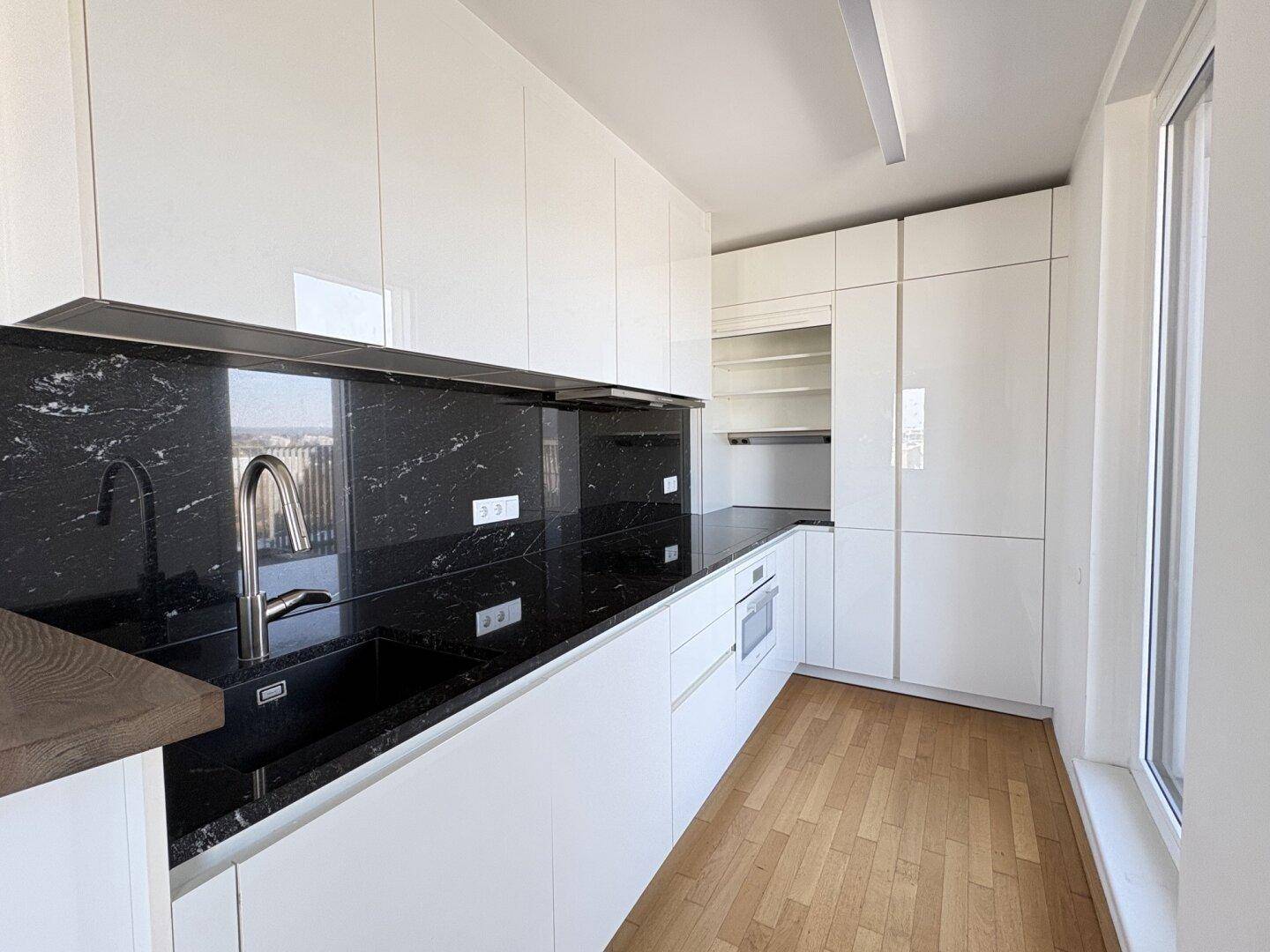 Elegante Einbauküche mit weißen Schränken, schwarzen Granitarbeitsplatten und integriertem Backofen.