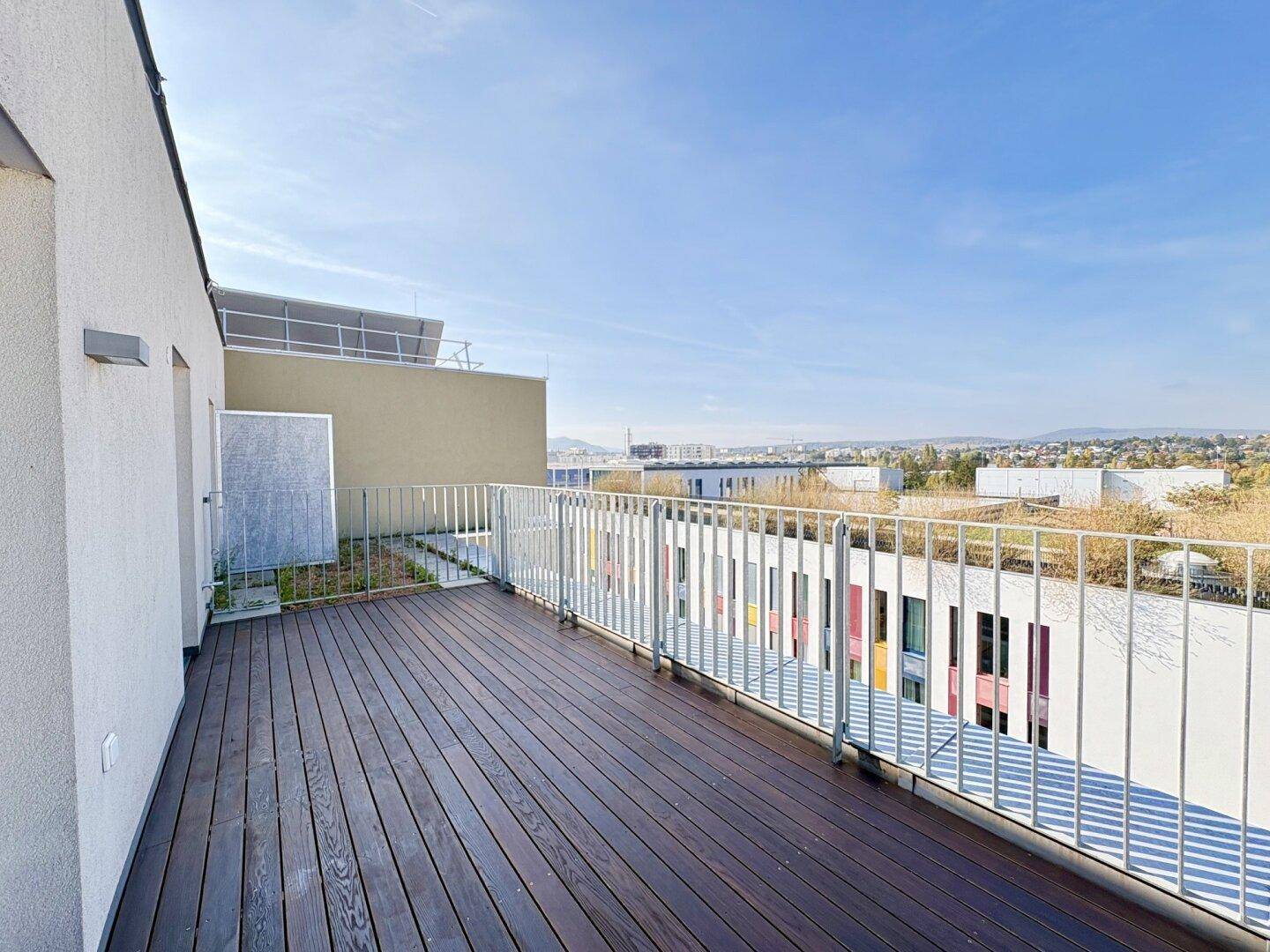 Geräumiger Balkon mit Holzboden und Blick auf die umliegenden Gebäude und Grünflächen.