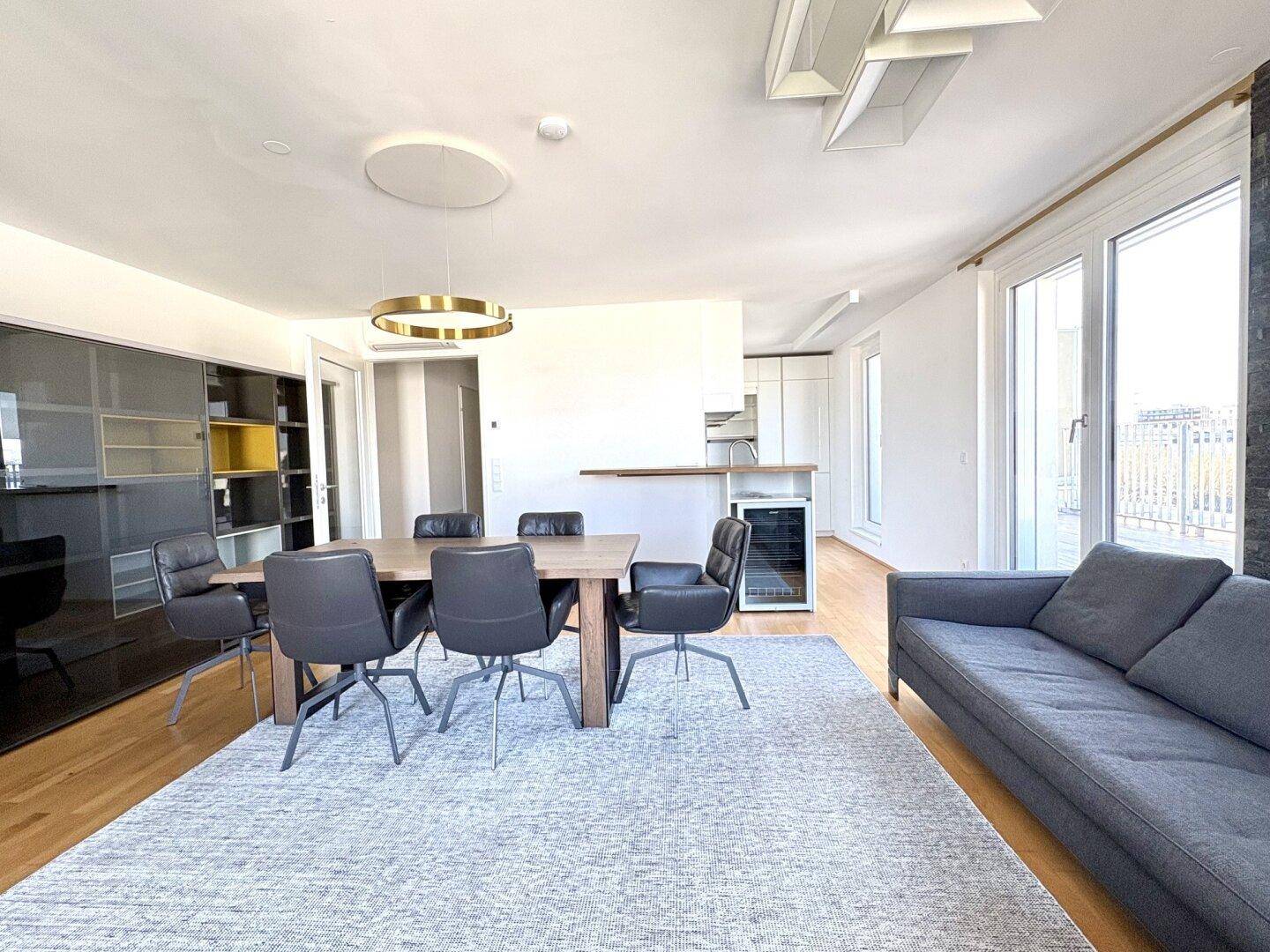 Heller Wohn-Essbereich mit Sofa, Esstisch und offener Küchenzeile im Hintergrund.