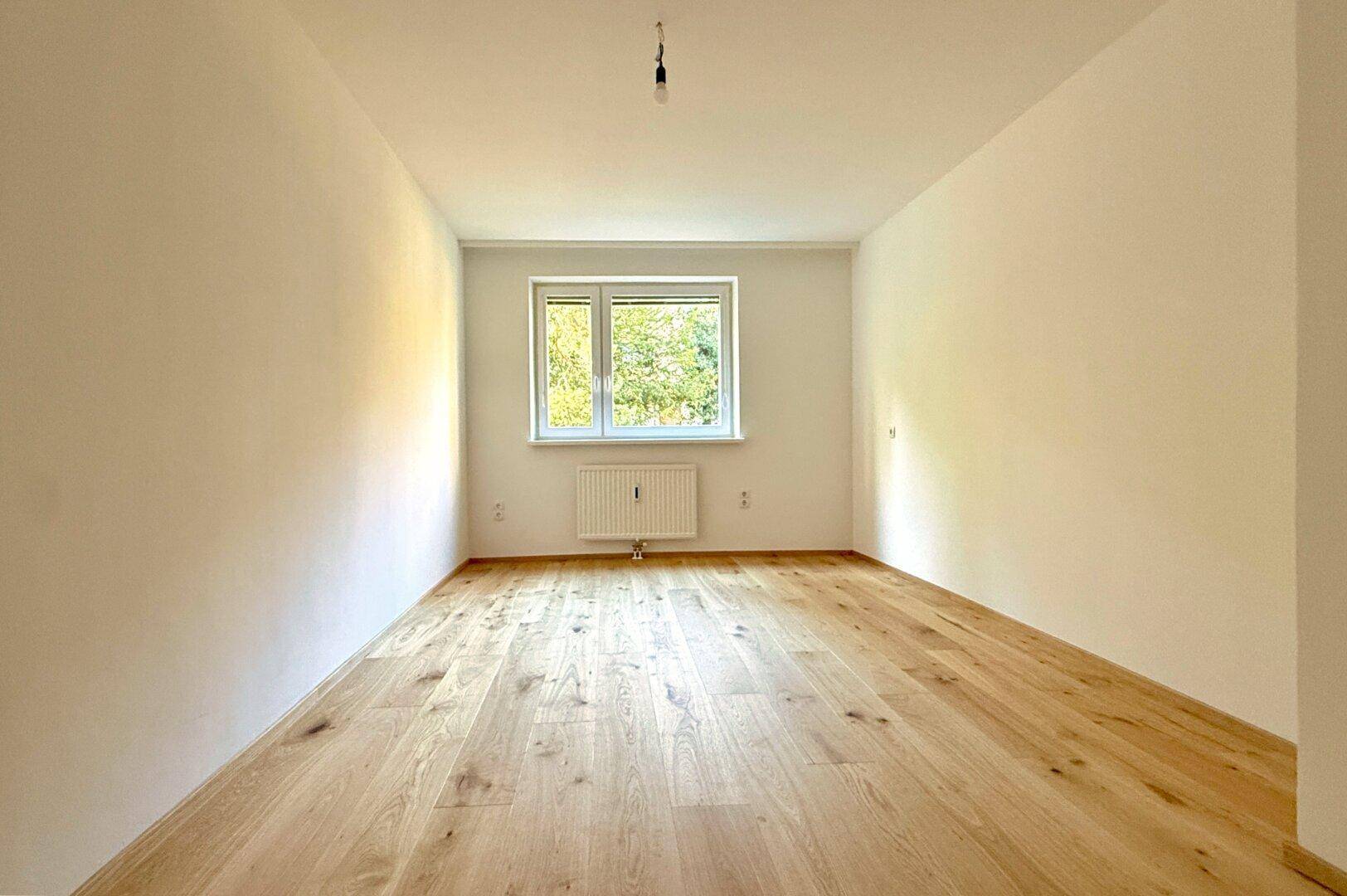 Heller Raum mit Holzboden und Fenster, bietet viel Tageslicht und eine ruhige Atmosphäre.