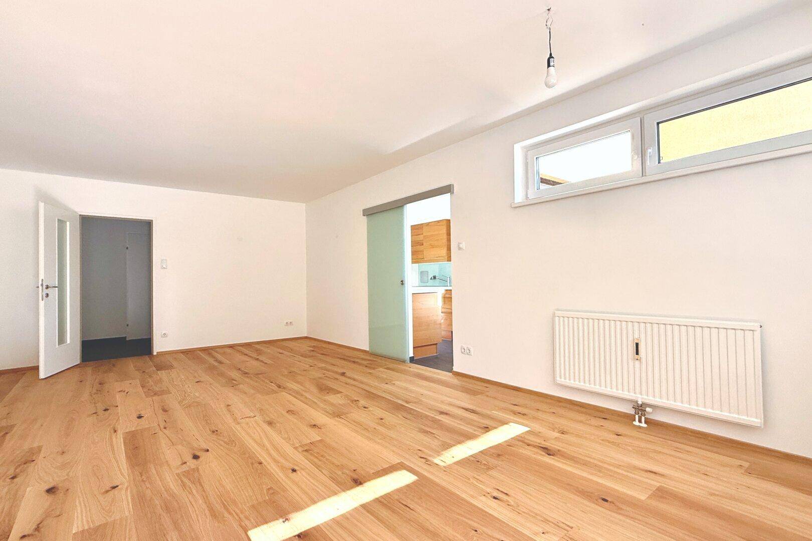 Heller Raum mit neuem Holzboden und Schiebetür zur Küche, ideal als Wohnbereich.