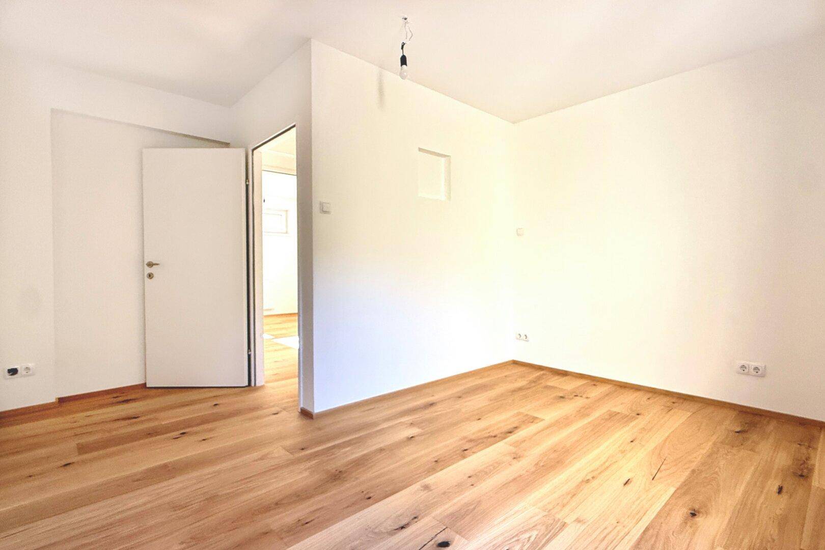 Leerer Raum mit hellem Holzboden und weißen Wänden, ideal als Schlaf- oder Arbeitszimmer.