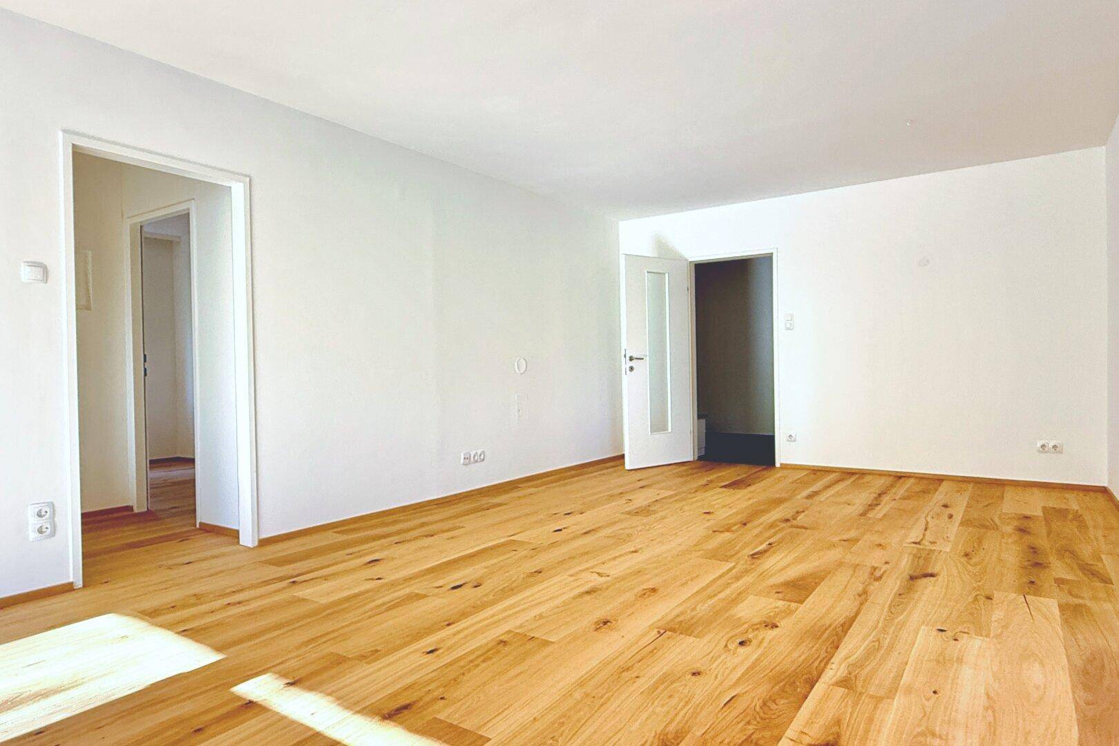 Geräumiger, heller Raum mit Holzboden und zwei Türen, bereit zur individuellen Gestaltung.