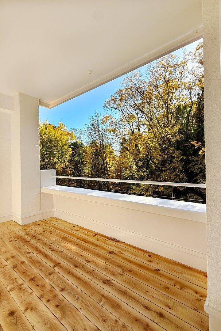 Heller Balkon mit Holzboden und weitem Blick auf die umliegende, herbstliche Natur.