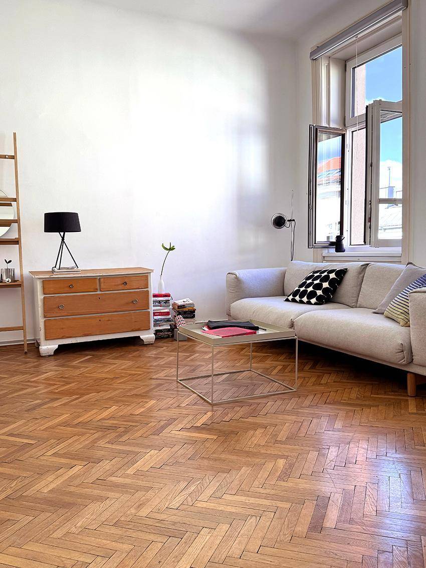 Detailansicht des hellen Wohnbereichs mit beigem Sofa, Couchtisch und Fischgrätparkettboden.
