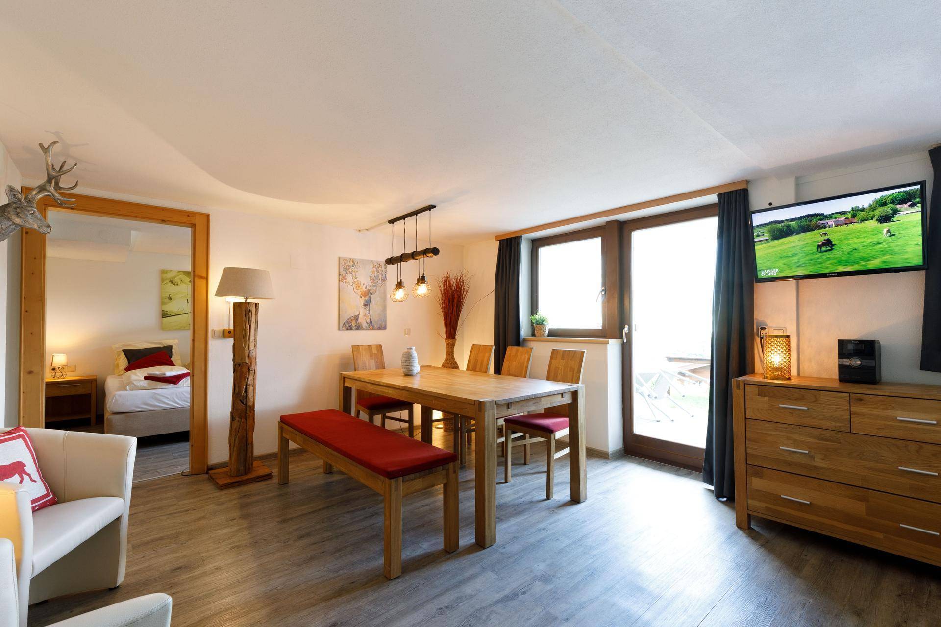 Heller Wohn-Essbereich mit Holztisch, bequemer Sitzbank und Zugang zu einem Balkon mit Aussicht.