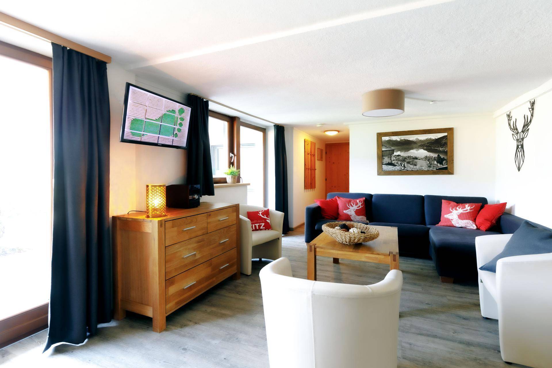 Modern eingerichtetes Wohnzimmer mit blauem Ecksofa, Holztisch und großen Fenstern für viel Tageslicht.