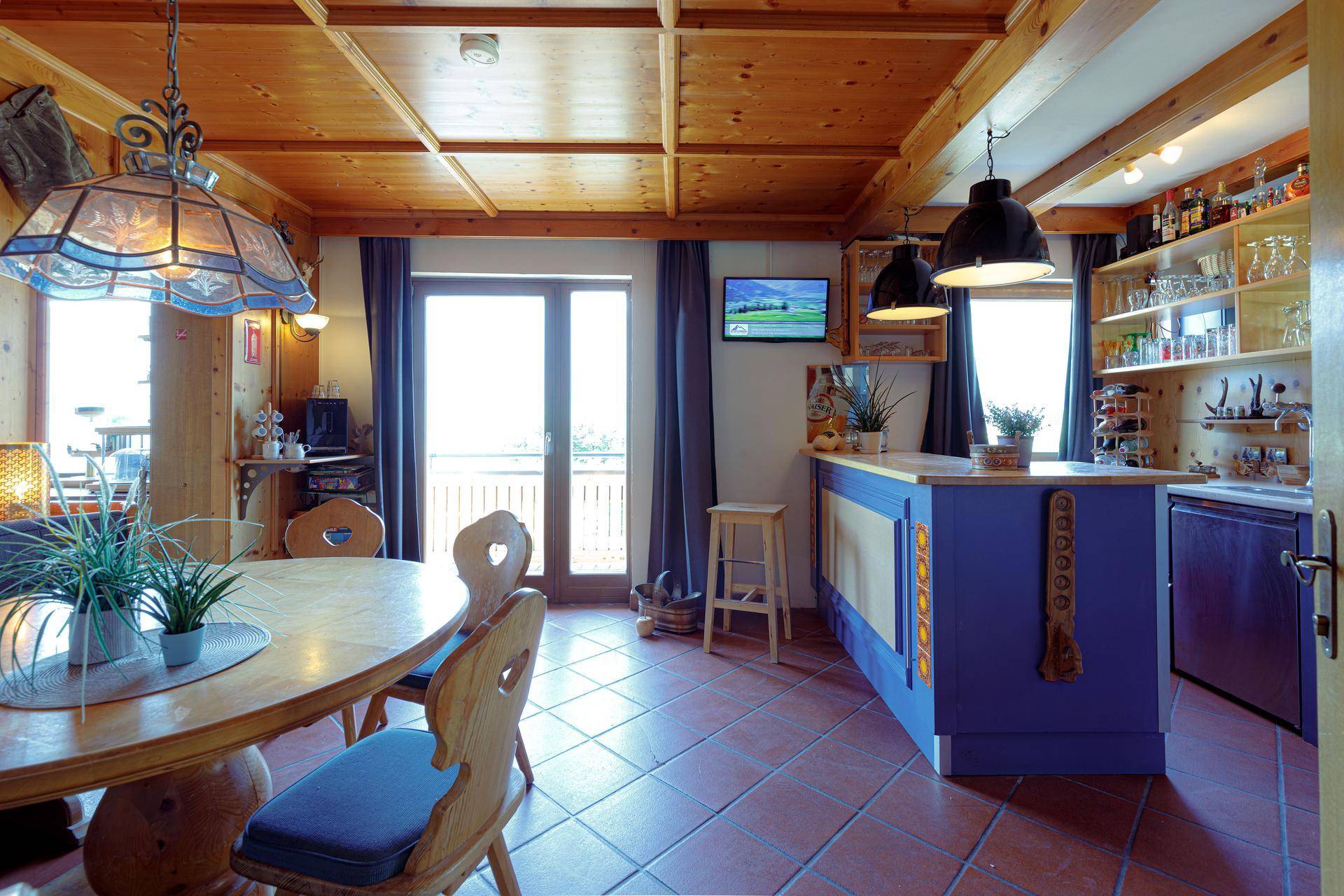 Rustikale Küche mit blauer Kücheninsel, Esstisch und Zugang zu einem Balkon mit Bergblick.