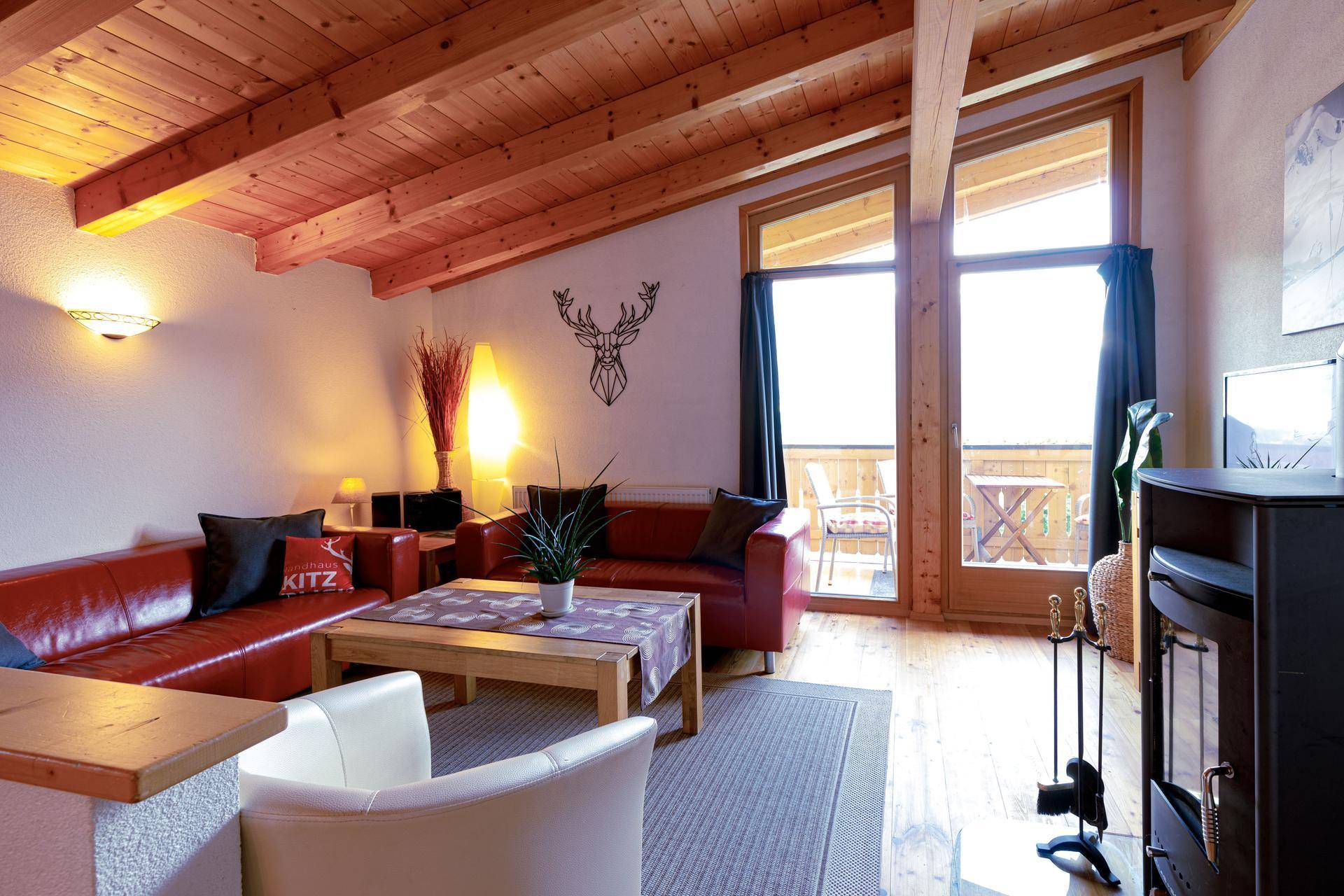 Gemütliches Wohnzimmer mit Holzbalkendecke, Ledersofas und Zugang zu einem Balkon mit Bergblick.