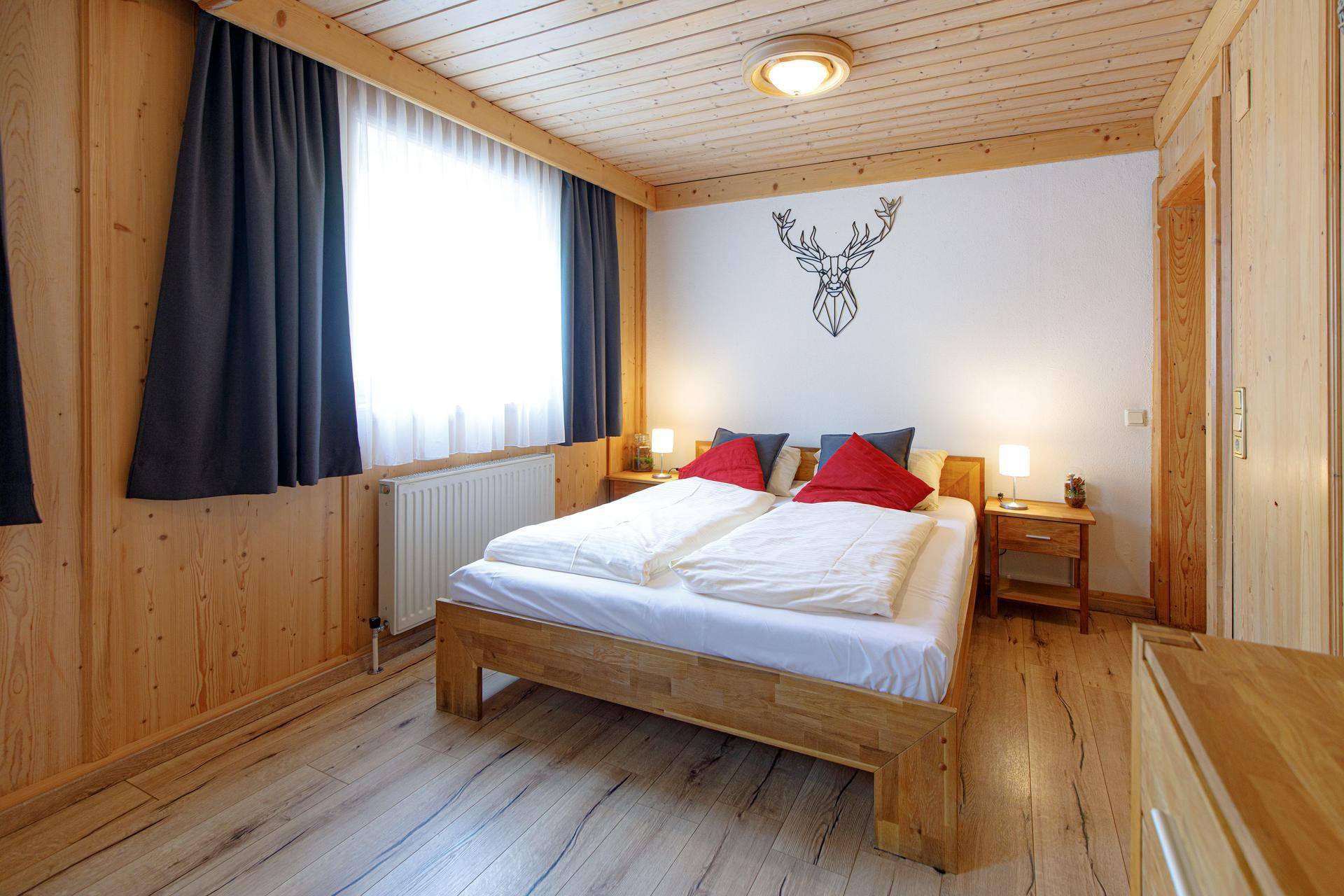 Gemütliches Schlafzimmer mit Holzbett, Holzwänden und Holzbalkendecke, die eine warme Atmosphäre schaffen.