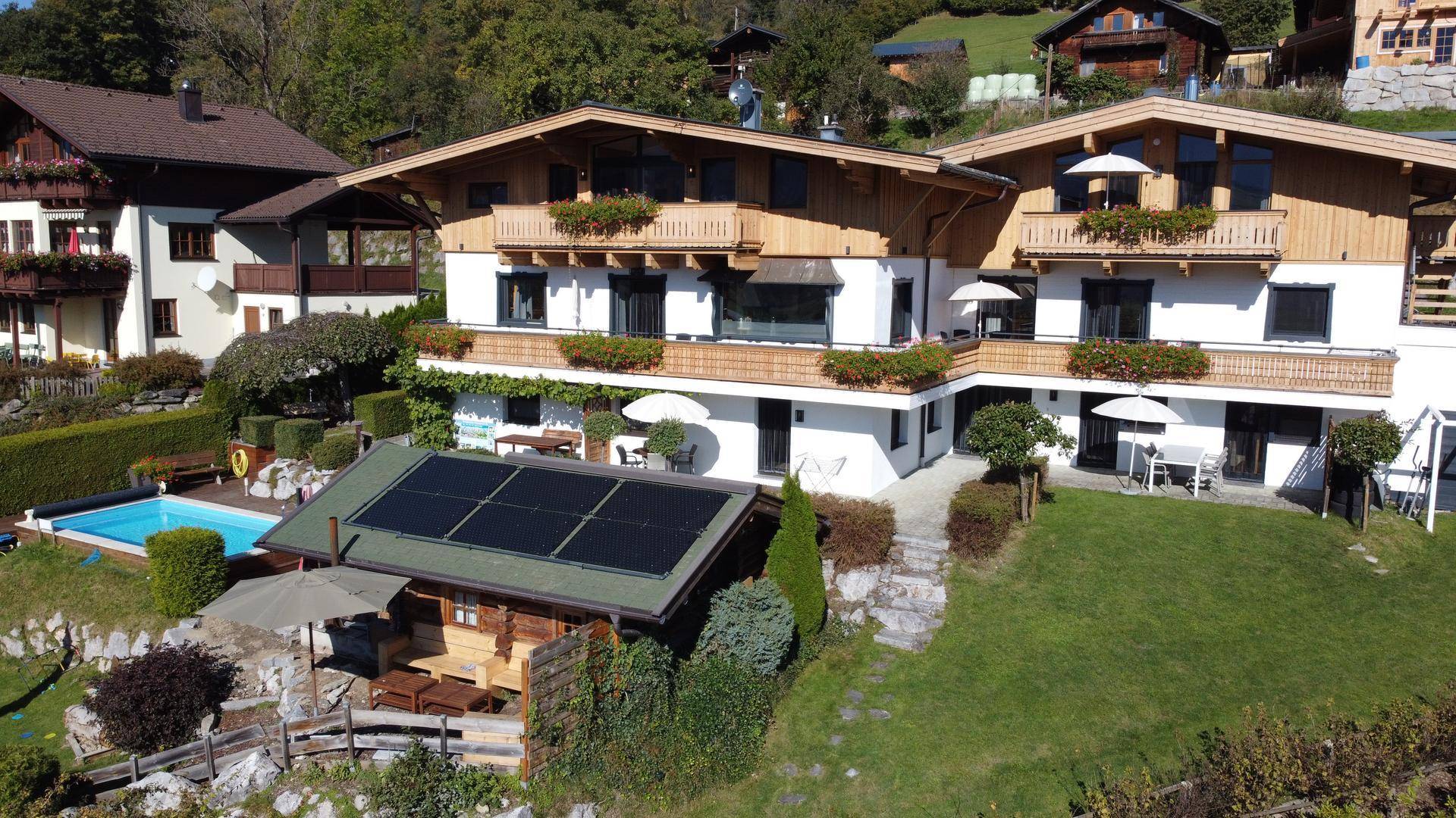 Großzügige Ferienanlage mit mehreren Gebäuden, Pool, Garten und Solaranlage auf dem Dach in alpiner Umgebung.