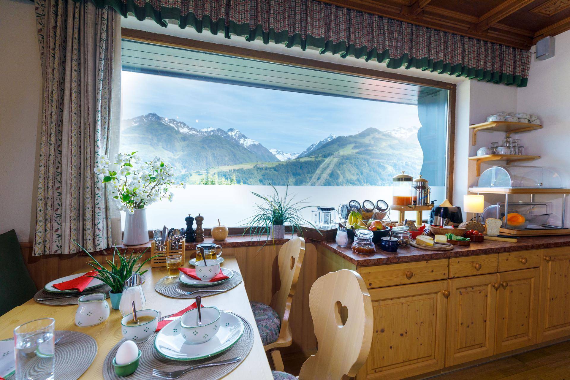 Frühstücksbereich mit Buffet, Holzküche und Panoramafenster mit atemberaubendem Blick auf die Berge und den See.