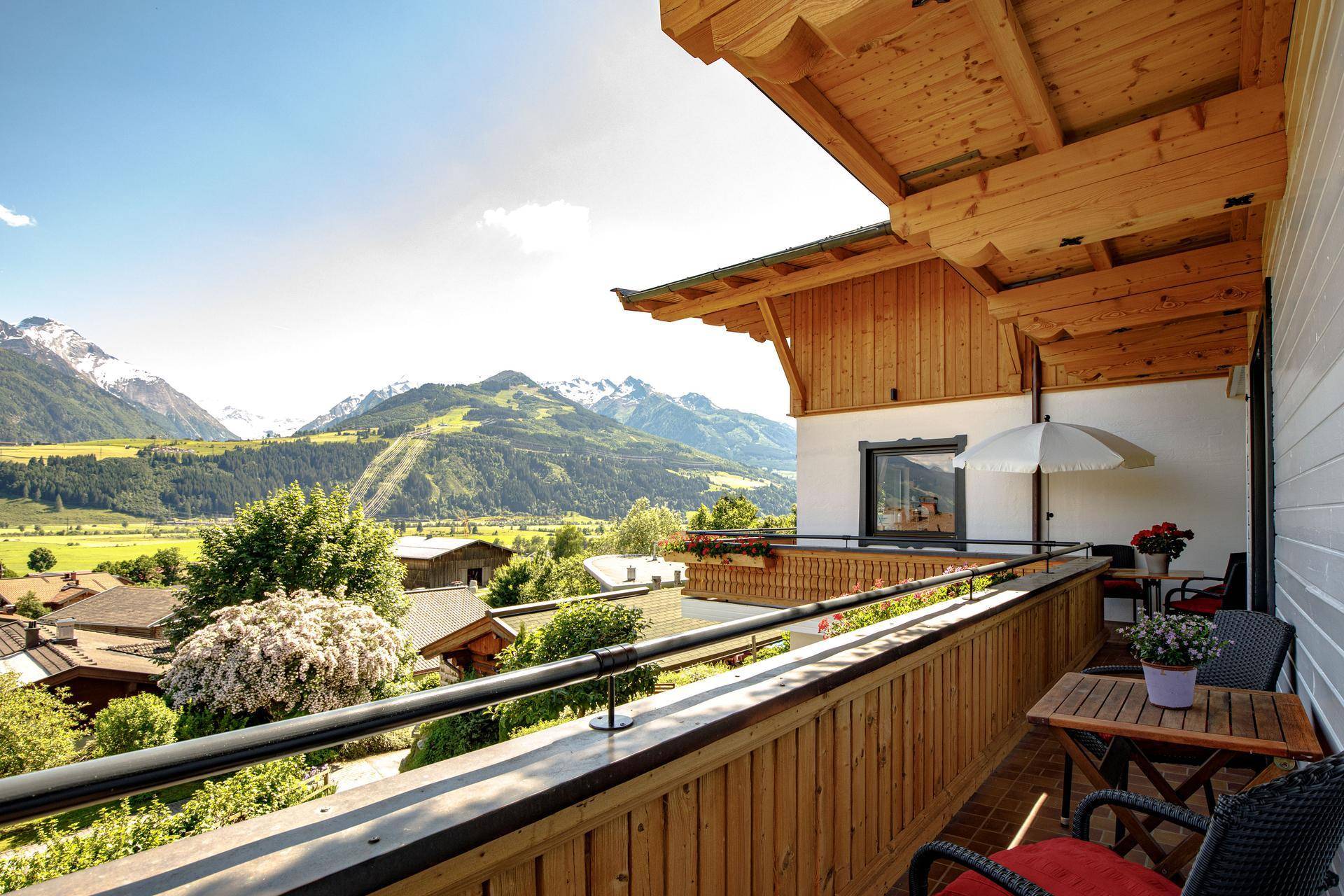 Geräumiger Balkon mit Holzgeländer, Sitzgelegenheiten und einem weiten Panoramablick auf die Berge.
