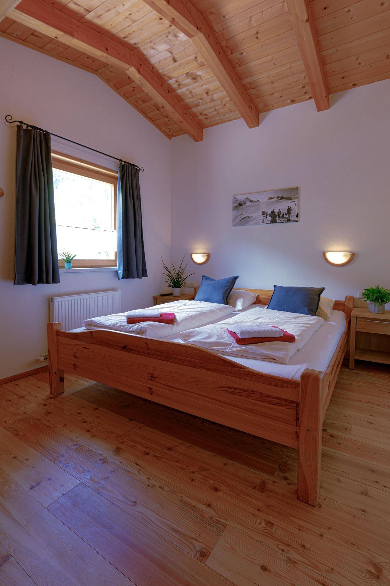 Helles Schlafzimmer mit Holzbett, Holzbalkendecke und einem Fenster, das viel Tageslicht hereinlässt.