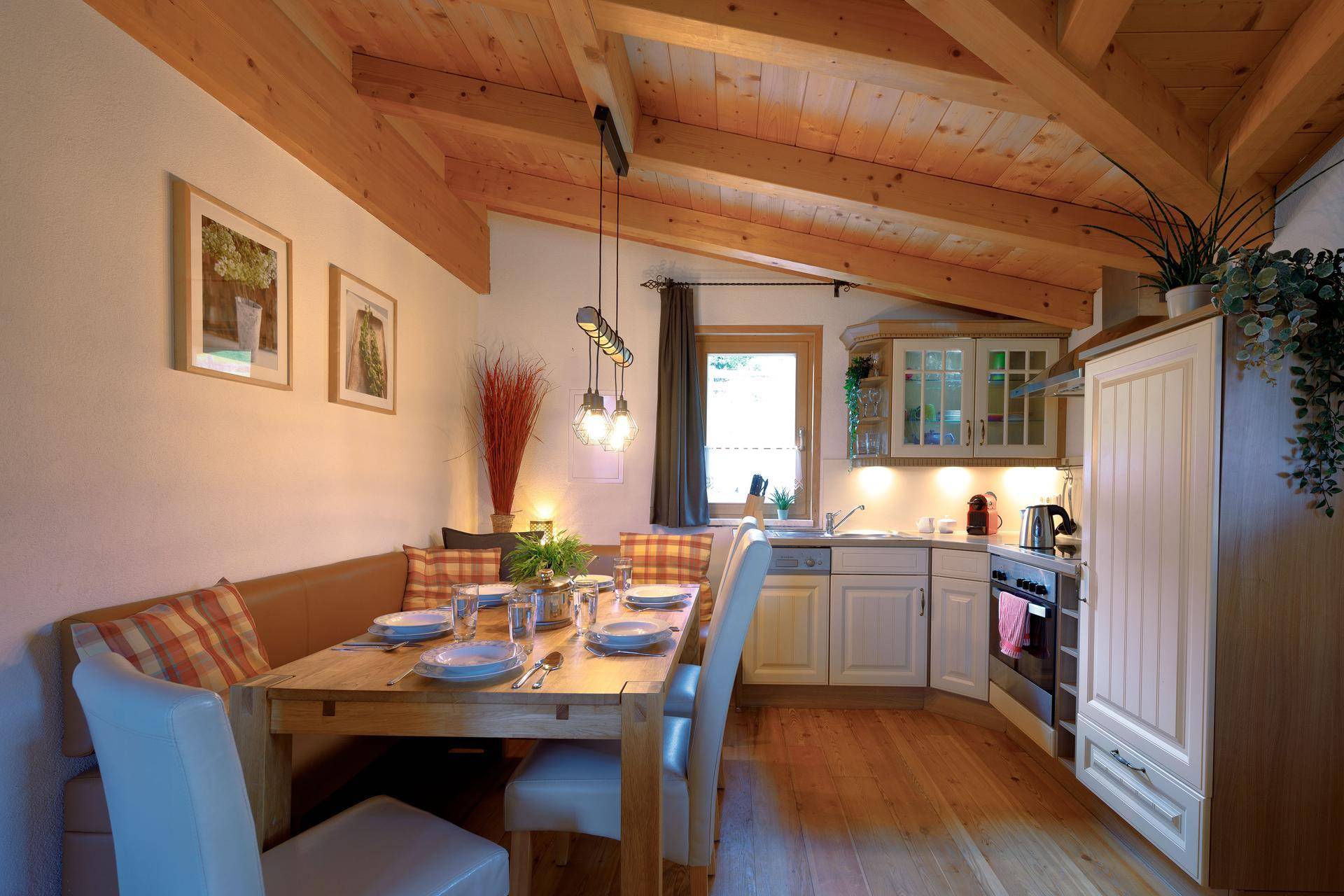 Helle Wohnküche mit Holzbalkendecke, Esstisch und einer kleinen Küchenzeile mit modernen Geräten.