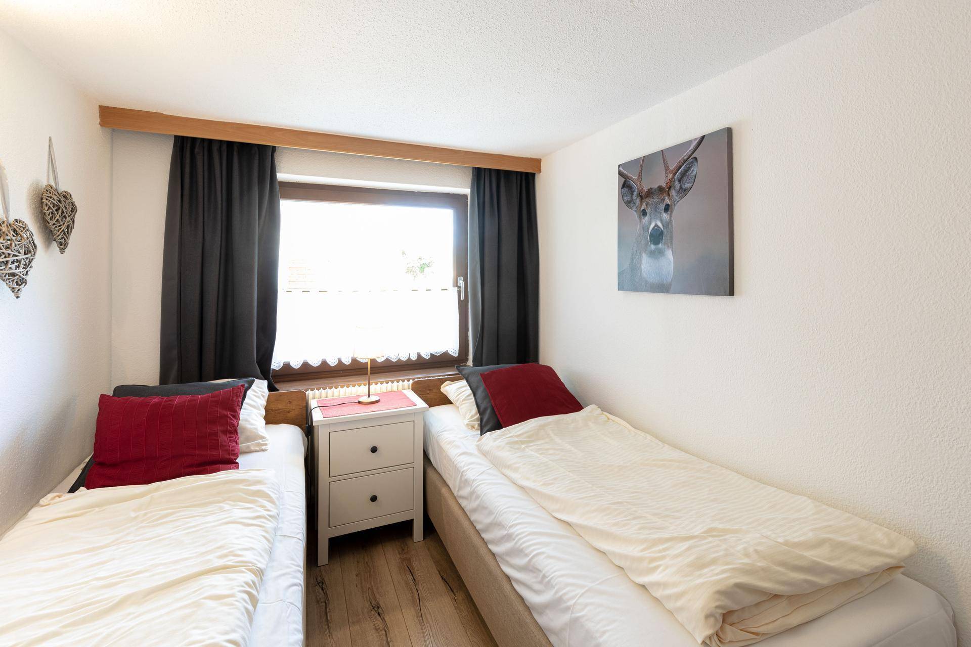 Komfortables Schlafzimmer mit zwei Einzelbetten, Holzboden und einem Fenster mit Blick ins Grüne.