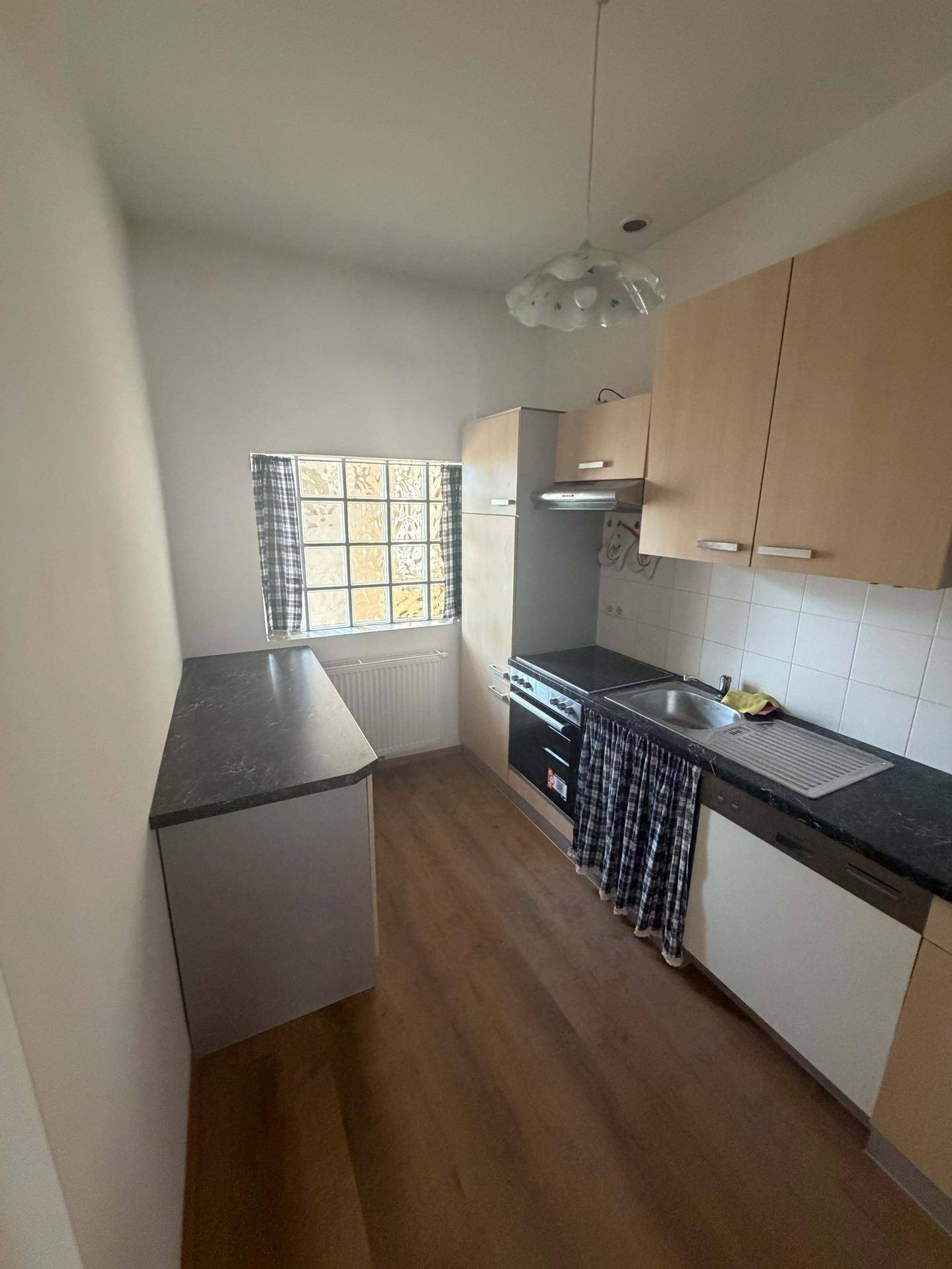 Funktionale Küche mit hellen Holzschränken, dunkler Arbeitsplatte und Fenster.