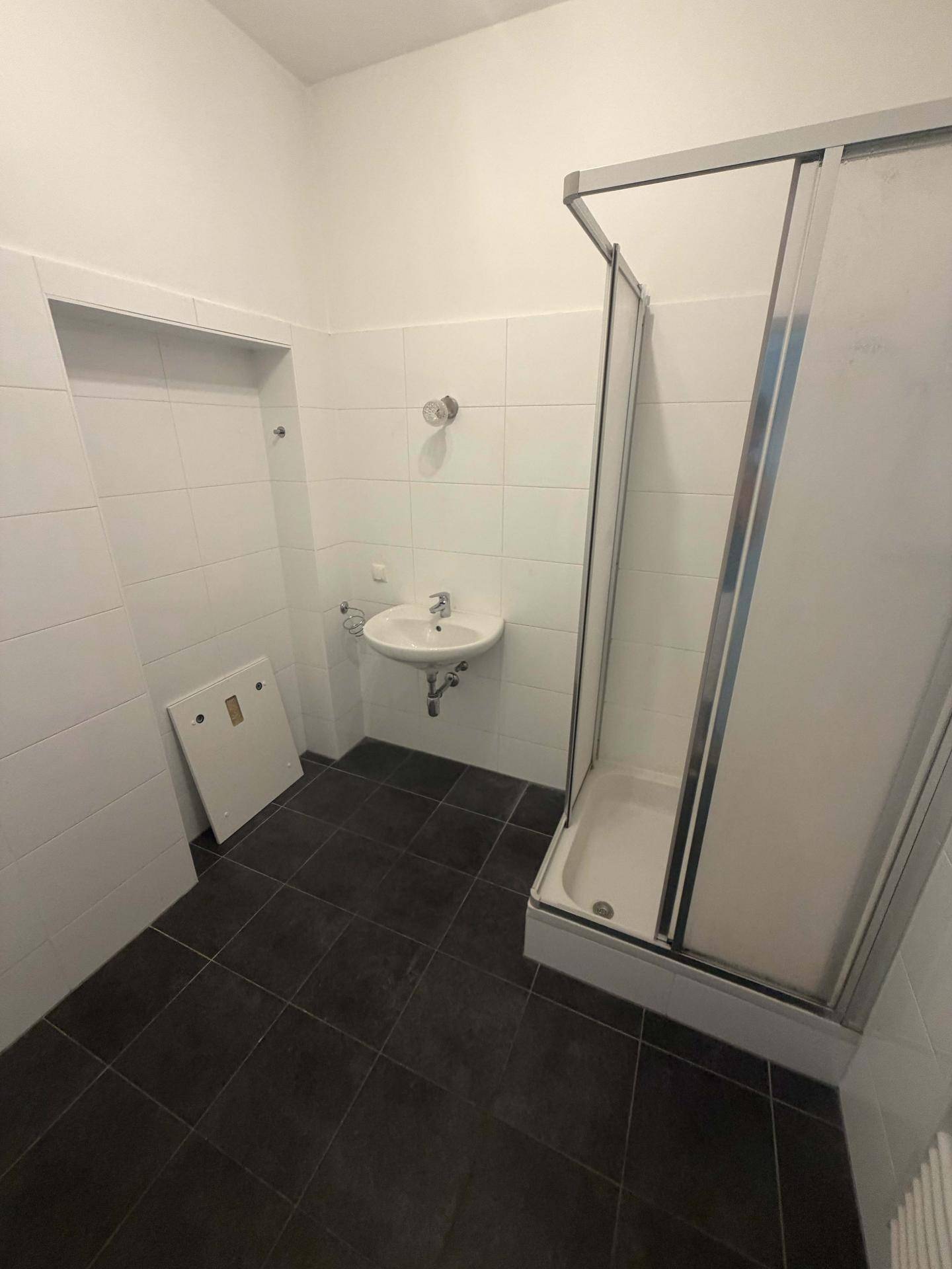 Badezimmer mit Duschkabine, Waschbecken und dunklen Bodenfliesen.