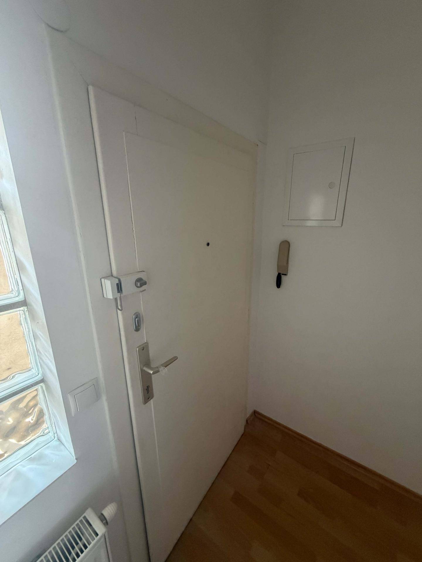 Eingangsbereich mit weißer Tür, Gegensprechanlage und Glasbausteinfenster.