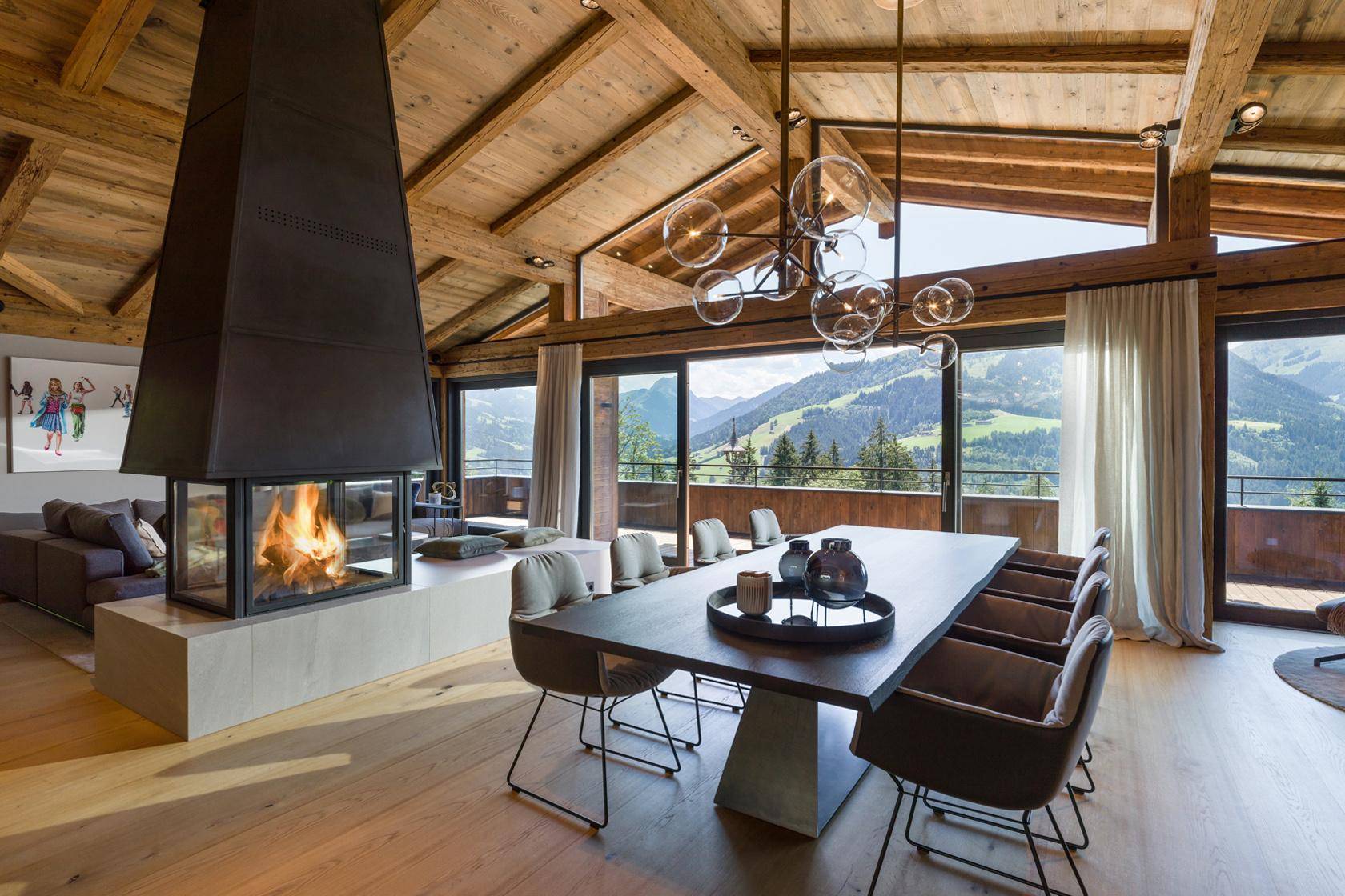 Eleganter Wohn-Essbereich mit Kamin, Holzbalkendecke und weitem Bergblick.