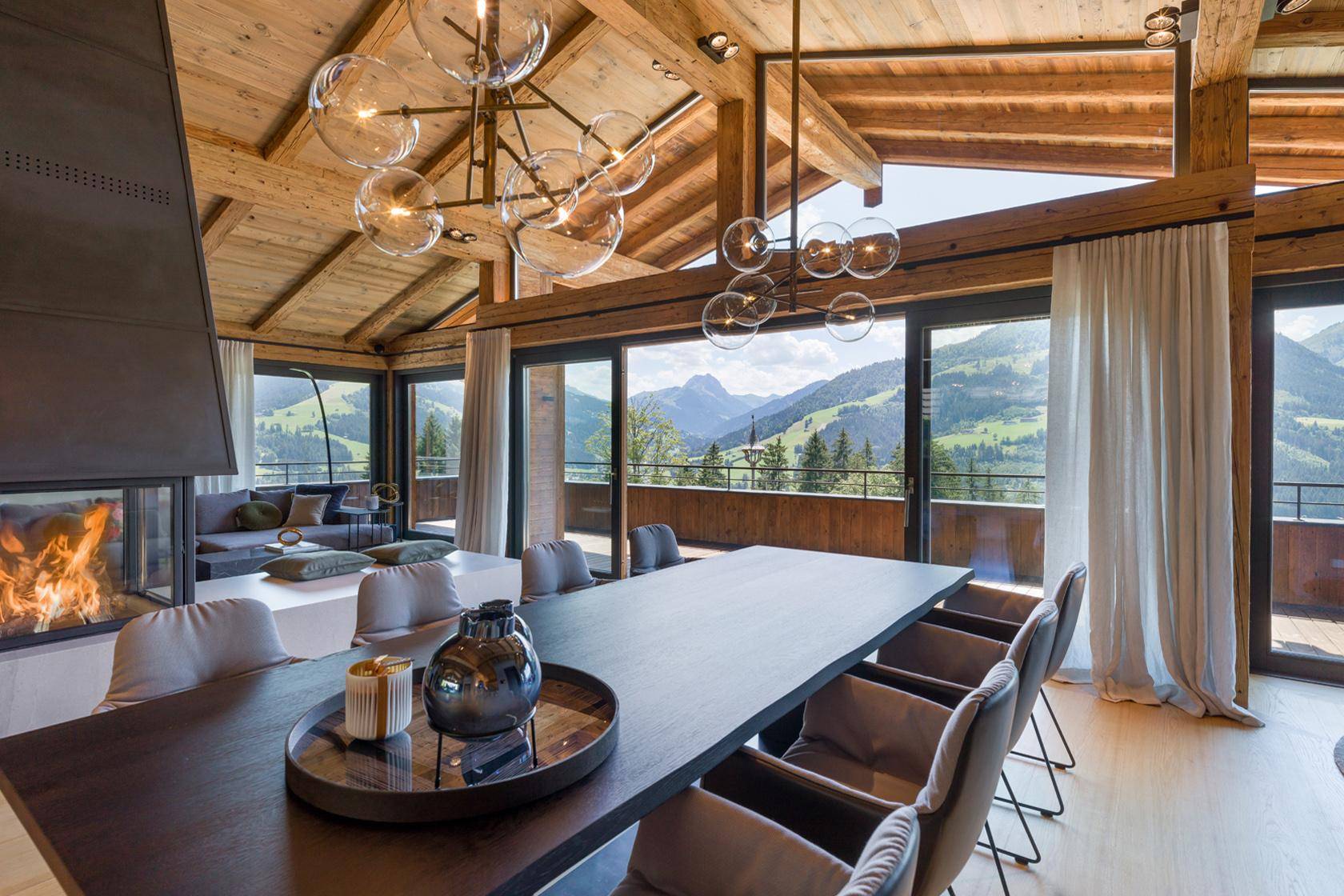 Stilvoller Essbereich mit großem Holztisch, Designerleuchten und beeindruckendem Bergblick.