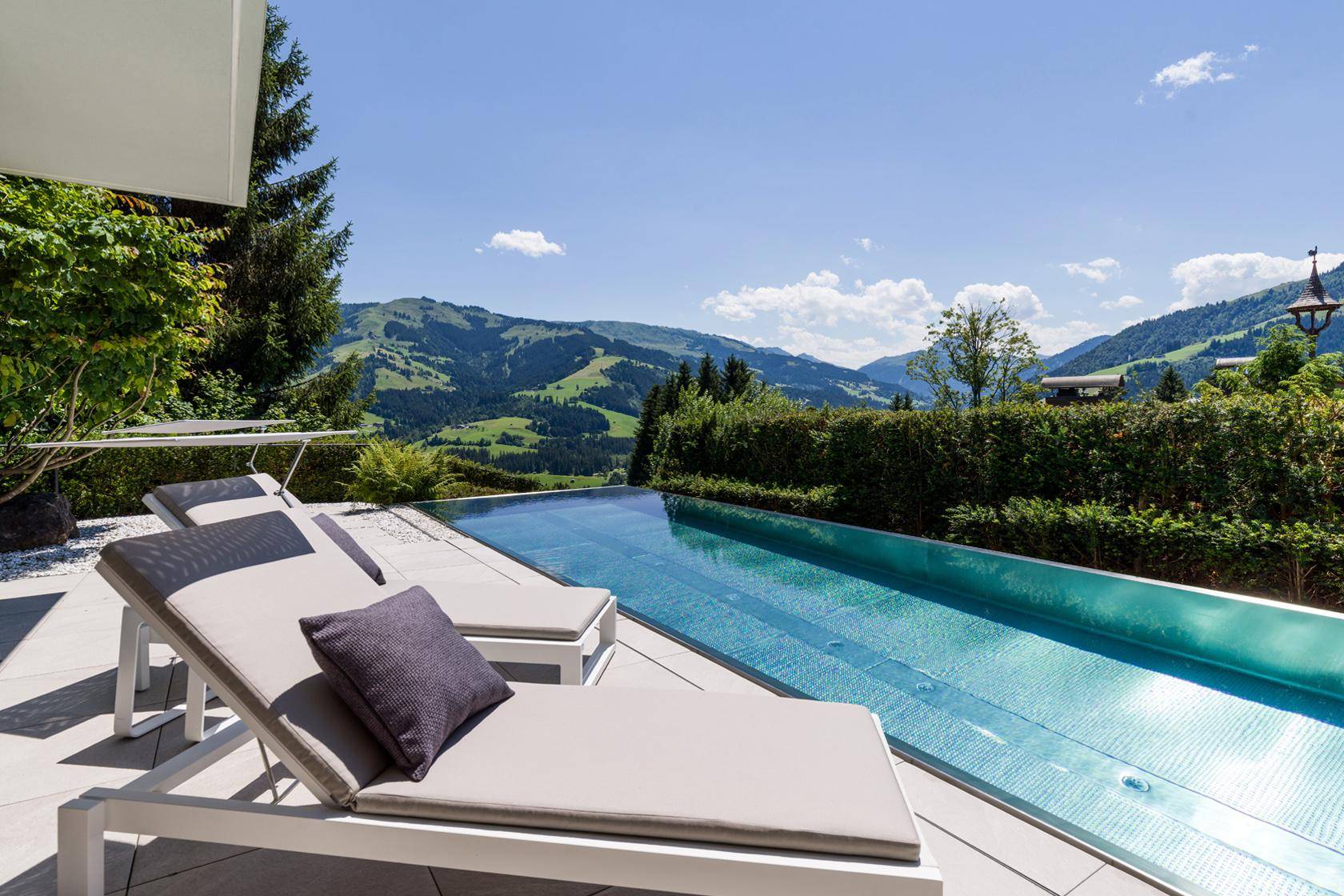 Sonniger Poolbereich mit Liegestühlen und Panoramablick auf die grüne Berglandschaft.