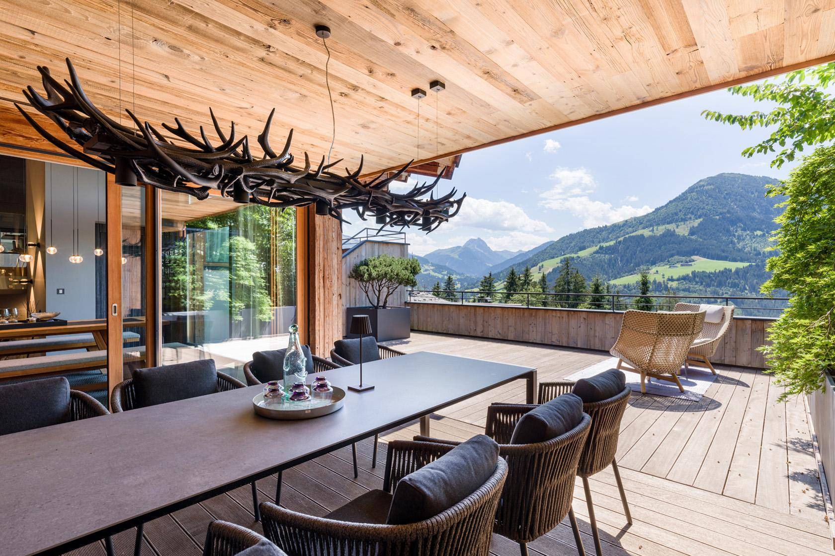 Große überdachte Terrasse mit Esstisch, Designerleuchte und weitem Bergblick.
