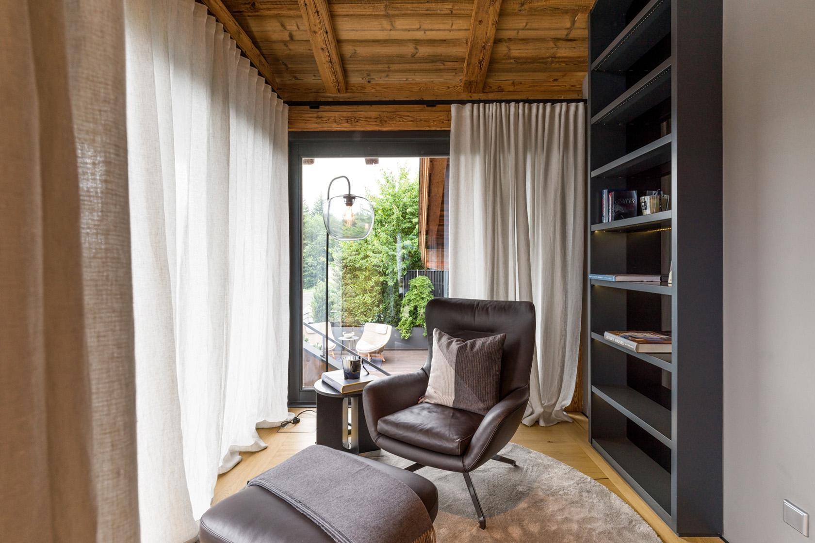 Gemütlicher Lesebereich mit Sessel, Bücherregal und Zugang zum Balkon.